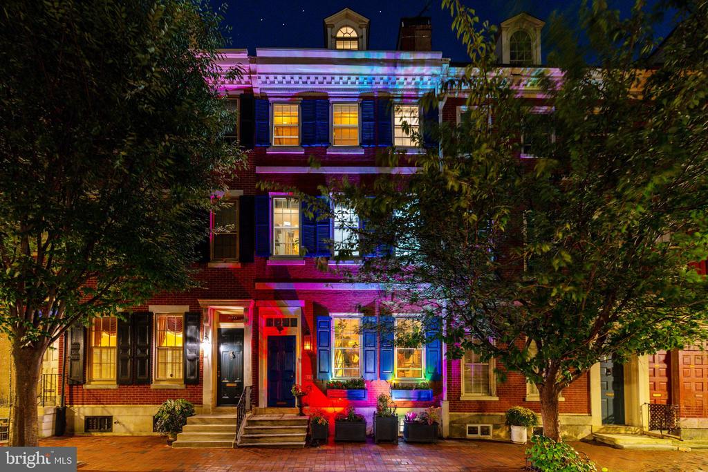 Red-brick townhouse at night with colorful facade lighting and illuminated windows.