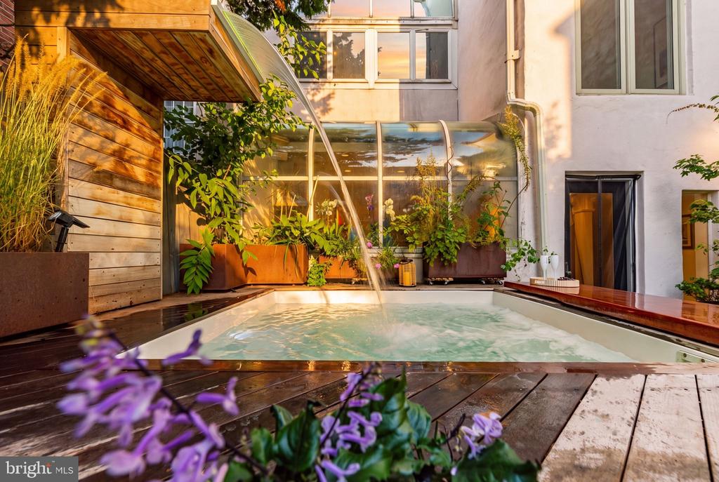 Courtyard pool with a wooden deck, lush planters, and a curved glass canopy.
