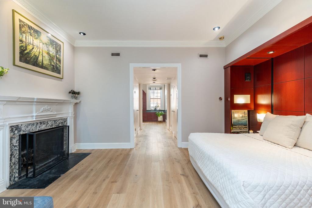 Bedroom with a marble-surround fireplace, light hardwood floors, and red built-in cabinetry.