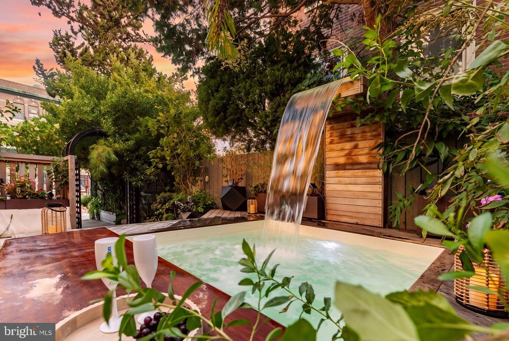 Backyard hot tub with a wooden waterfall feature, surrounded by lush greenery.