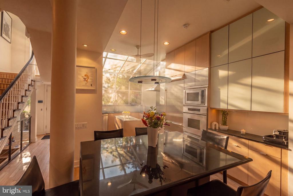 Modern kitchen and dining area with a glass ceiling, cream cabinetry, and a glossy dark dining table.