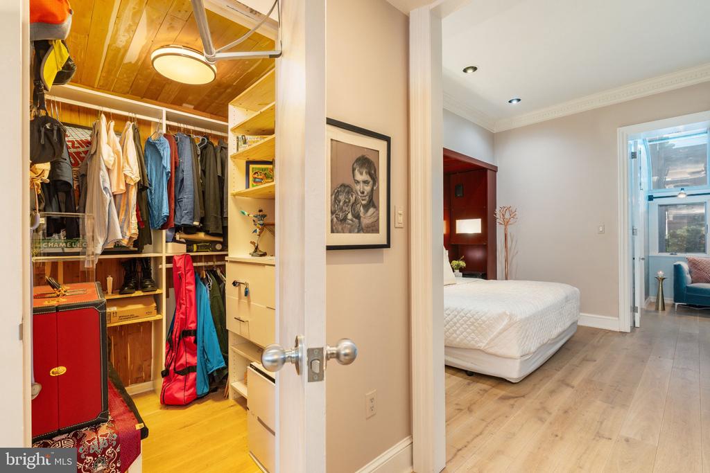 Bedroom with a white mattress and light wood floors beside an open walk-in closet with built-in shelving.