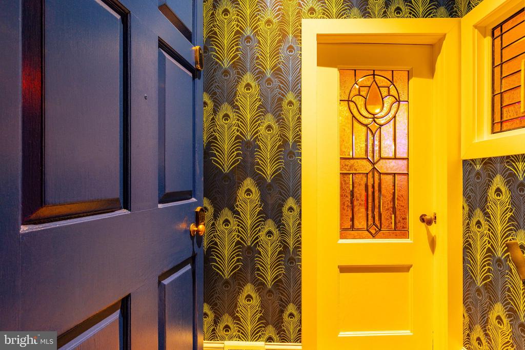 Entryway with blue and yellow doors, stained glass, and gold feather-patterned wallpaper.