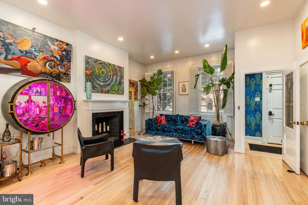 Living room with a fireplace, blue patterned sofa, colorful artwork, and a pink-lit round bar cabinet.