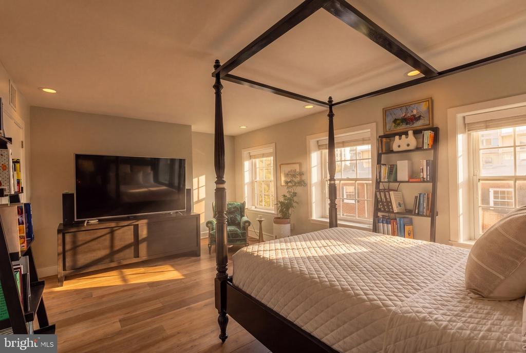 Bedroom with a four-poster canopy bed, hardwood floors, and sunlit windows.