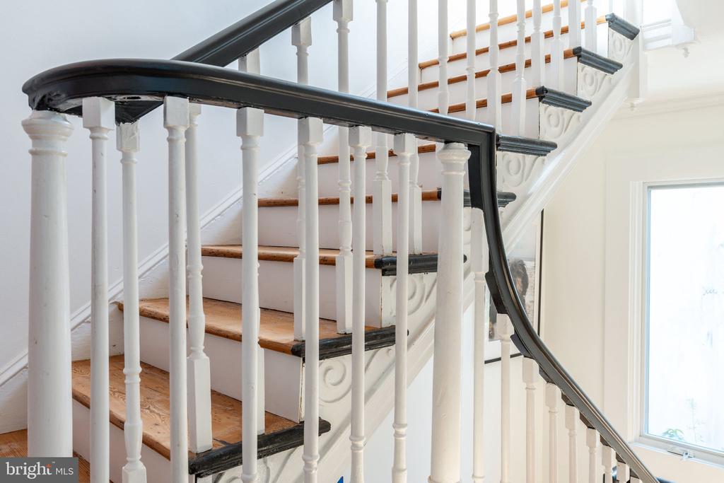 Interior staircase with wood treads, white balusters, and a dark curved handrail.