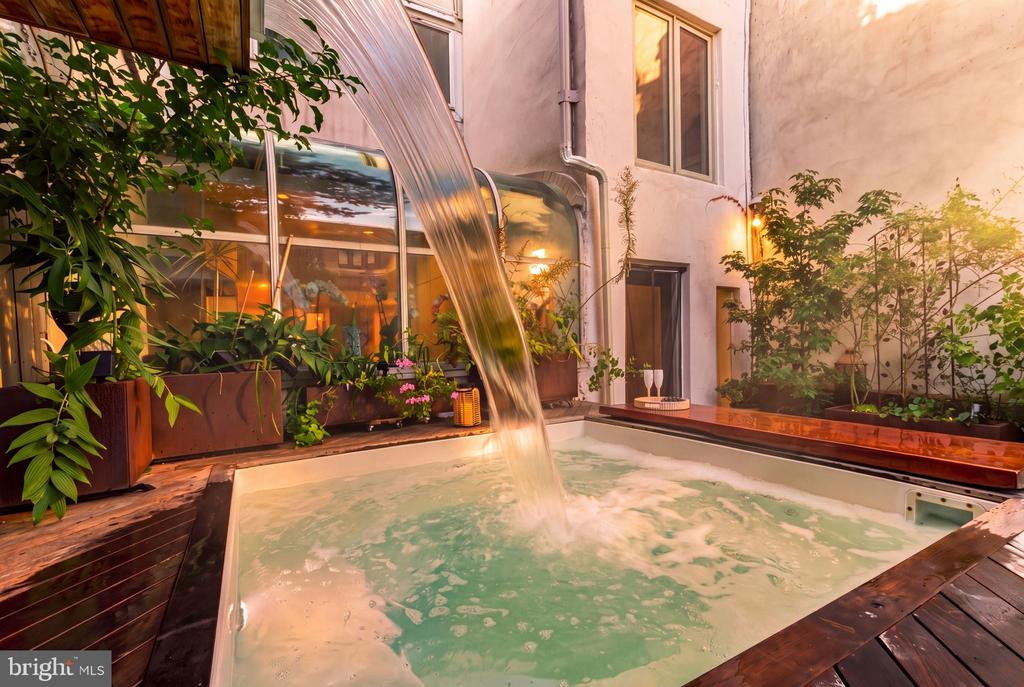 Courtyard hot tub with a cascading waterfall, lush plants, and a wooden deck.