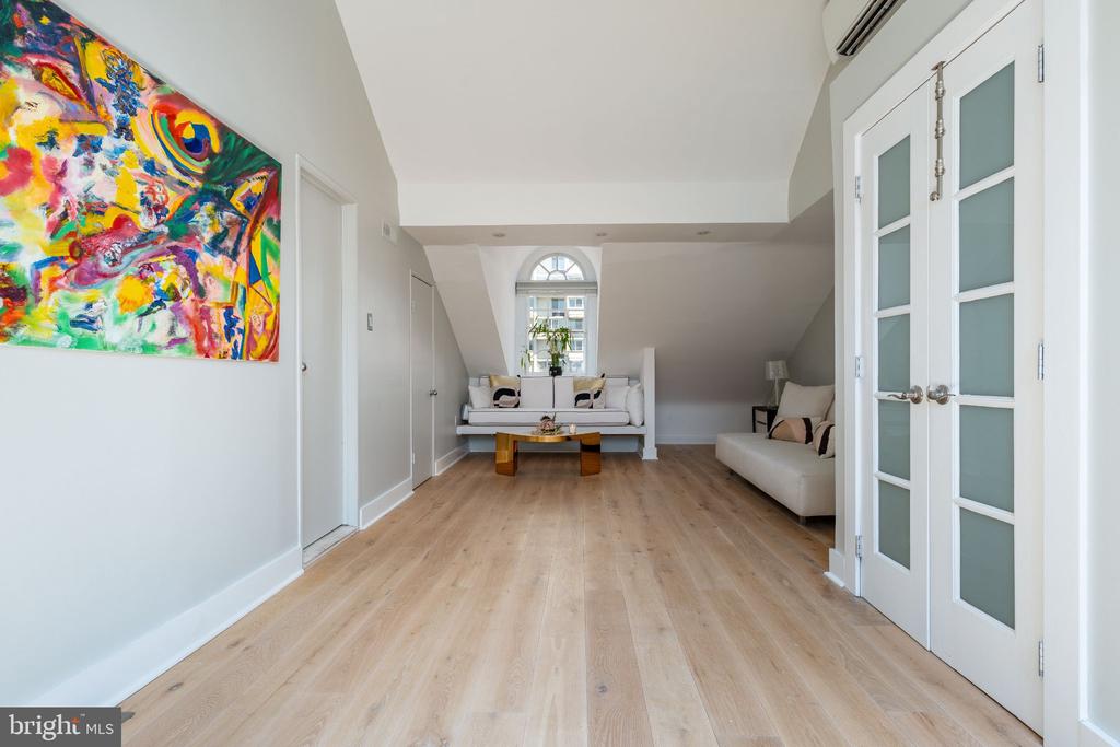 Living room with pale wood floors, white sofas, a colorful abstract painting, and French doors.