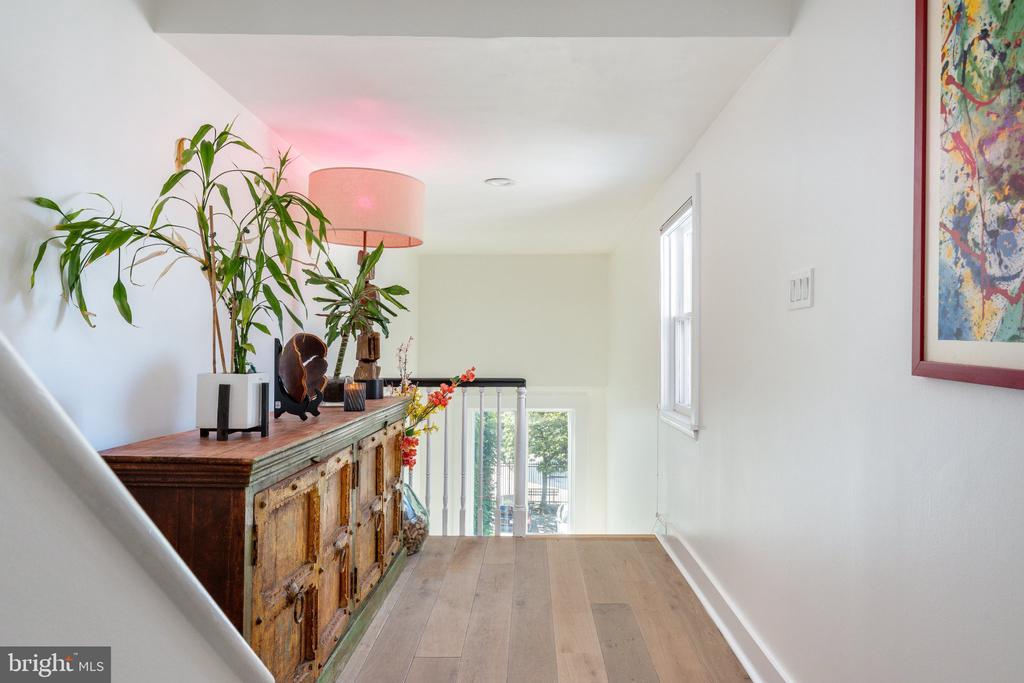 Upstairs landing with a rustic console, leafy plants, pink-shaded lamp, and light wood flooring.