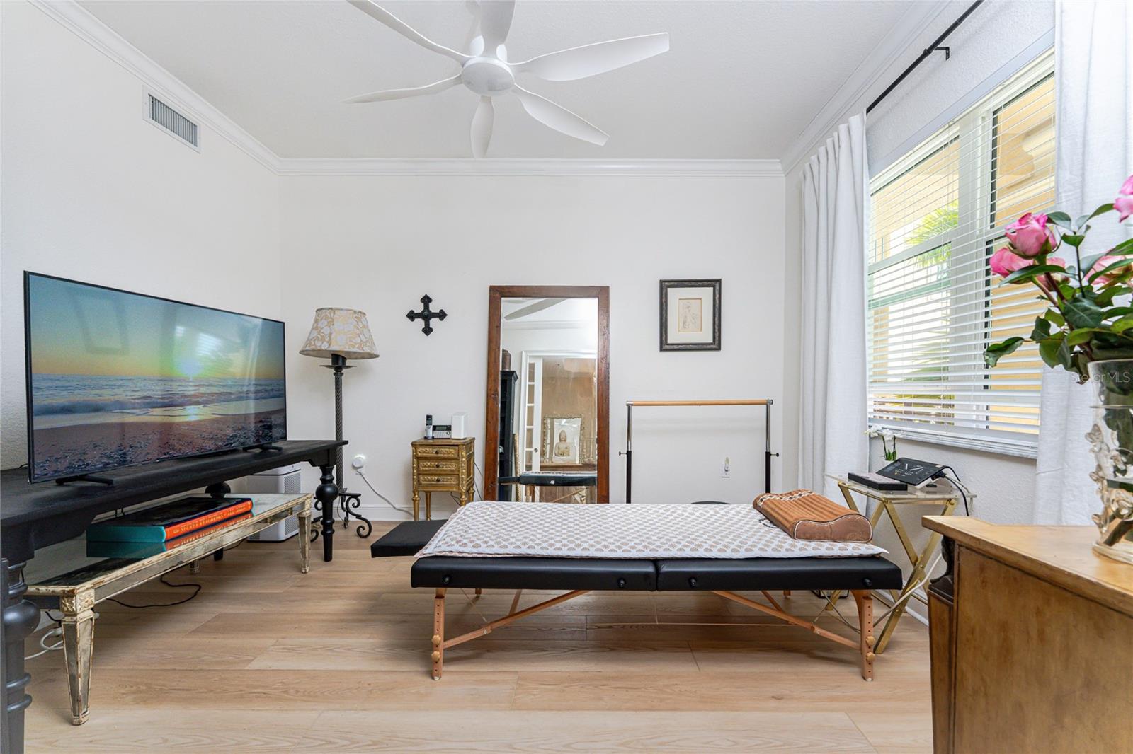 Furnished bedroom with a beach scene on the television and a large curtained window.