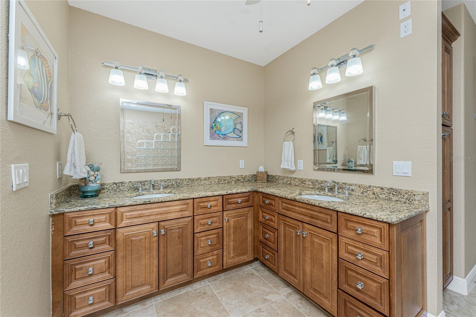 Bathroom with a double-sink granite vanity, warm wood cabinetry, and large mirrors.