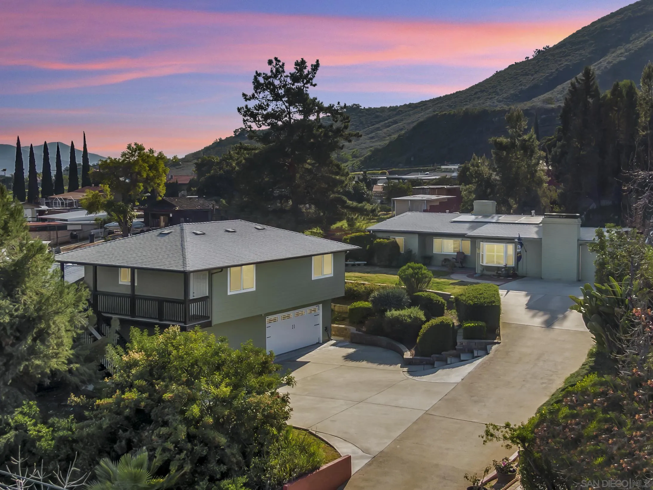 Two landscaped homes beneath hillside ridges at dusk, with a pink sunset sky.