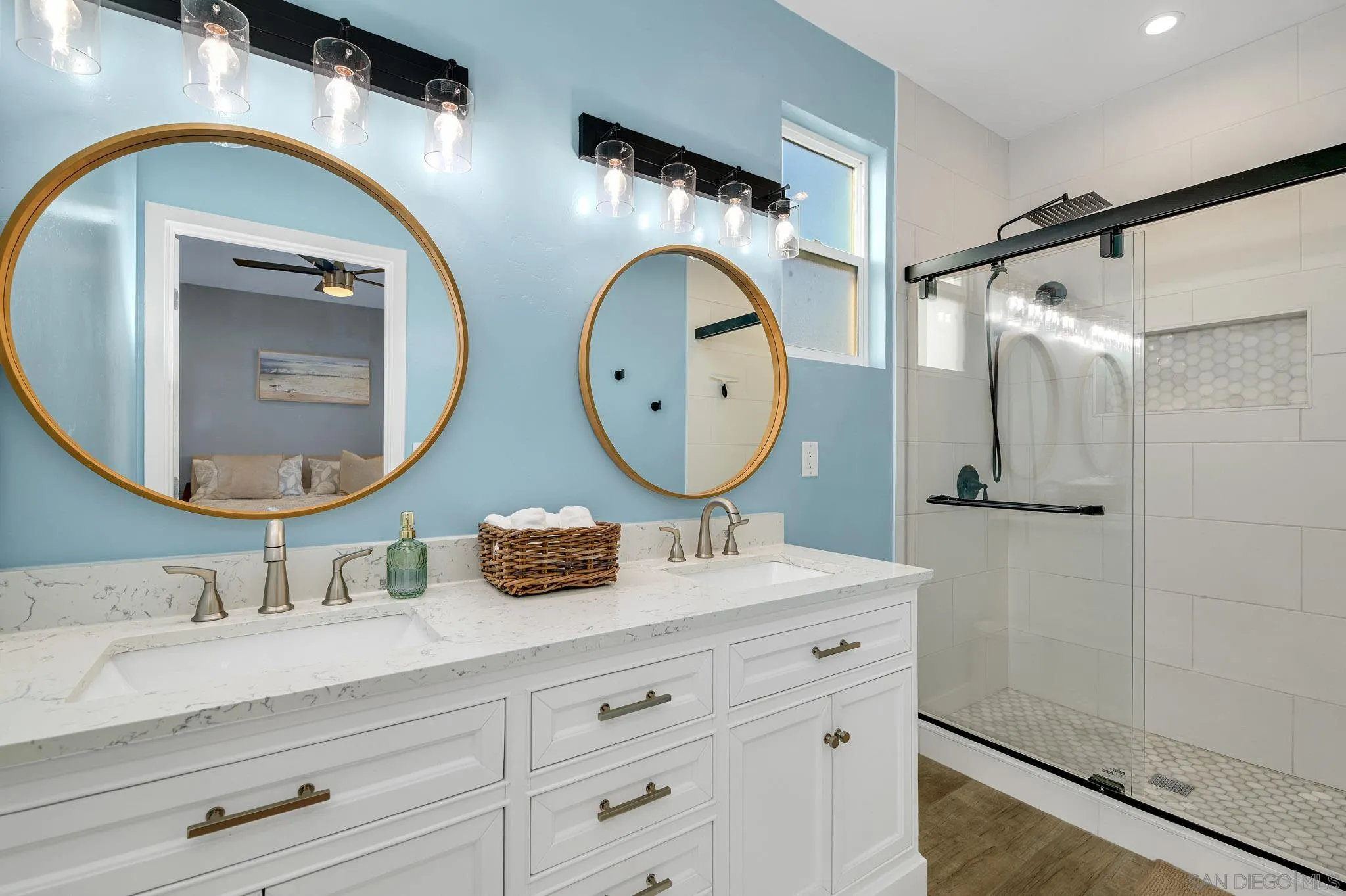 Bathroom with a white double vanity, round gold-framed mirrors, and a glass walk-in shower.