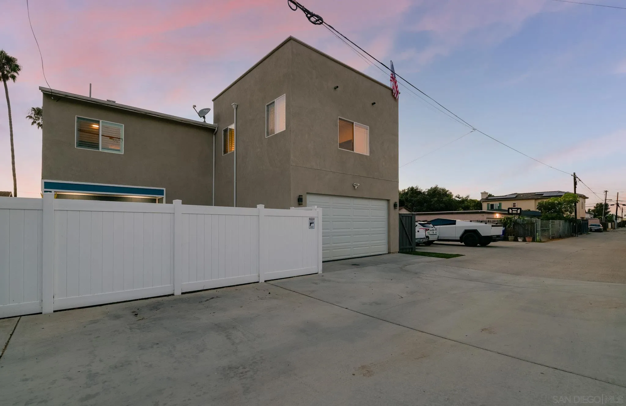 Two-story gray house with a white privacy fence and garage at dusk.