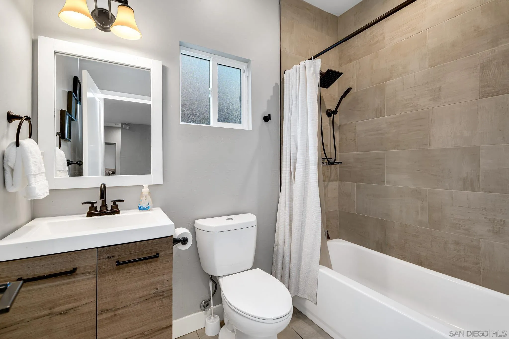 Bathroom with a wood vanity, white fixtures, and a tan tiled tub surround.
