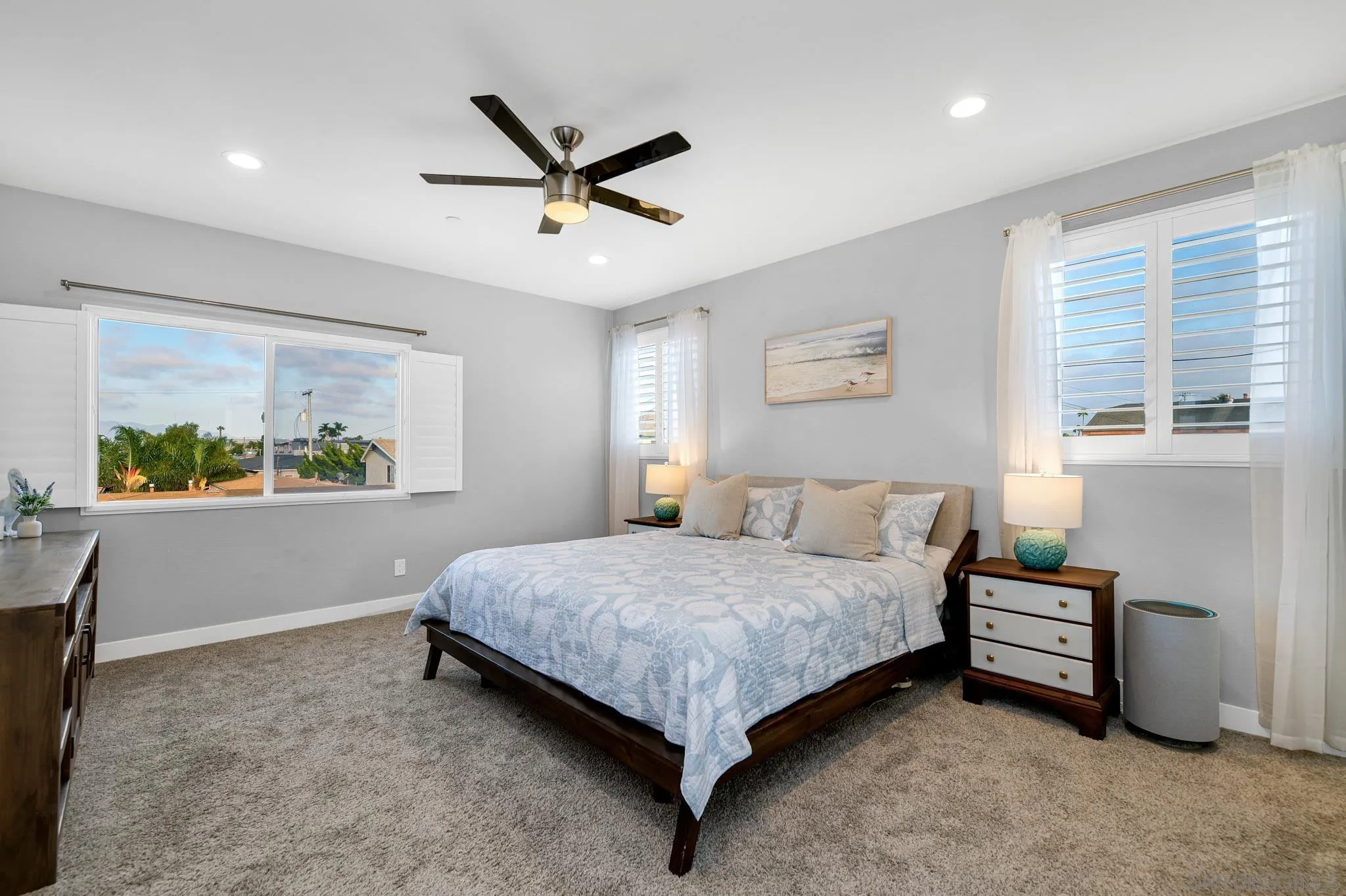 Staged bedroom with pale blue bedding, shuttered windows, and a dark wood bed.