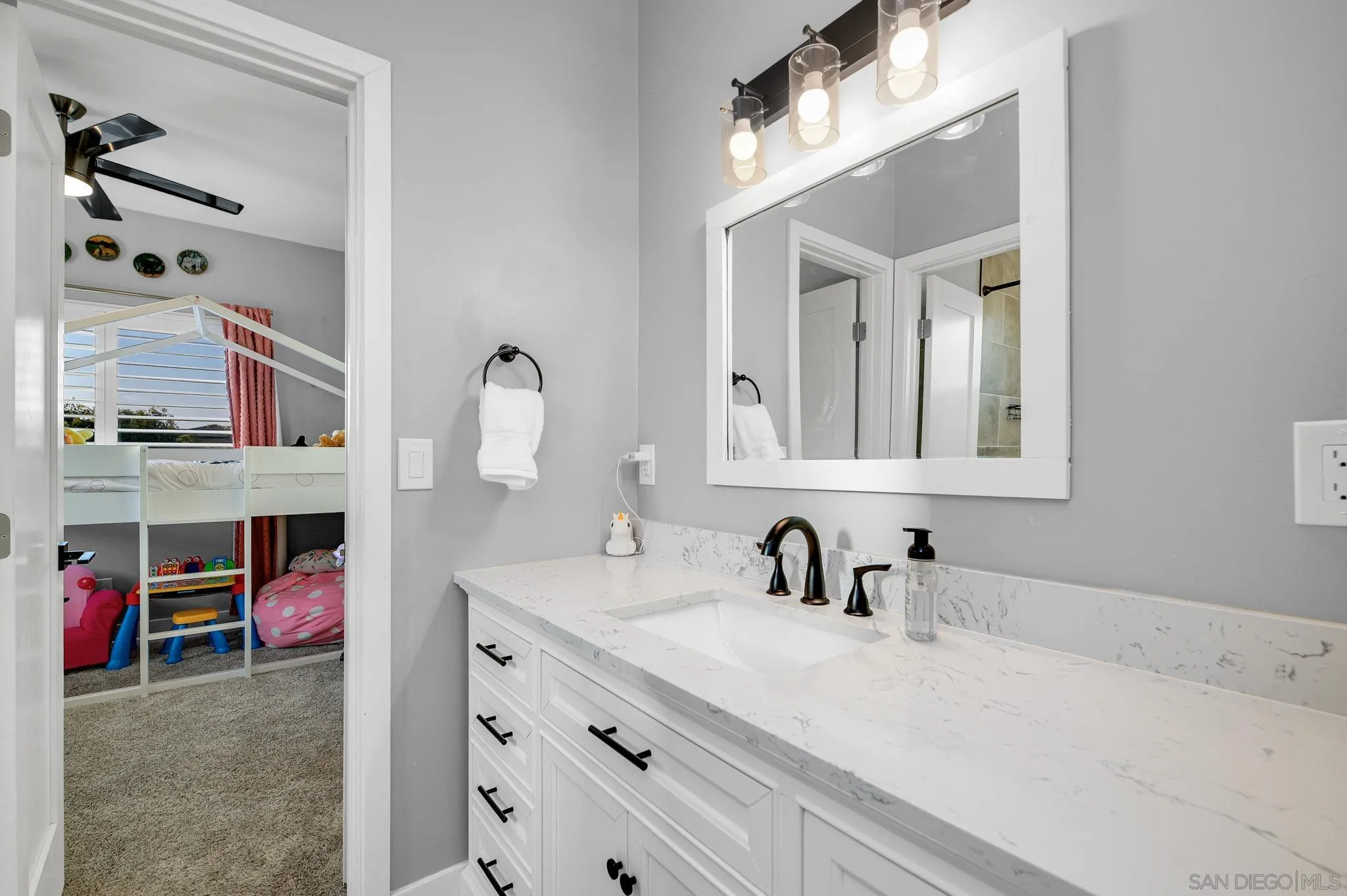 Updated bathroom with a long white vanity and black faucet, looking into a child’s bedroom.