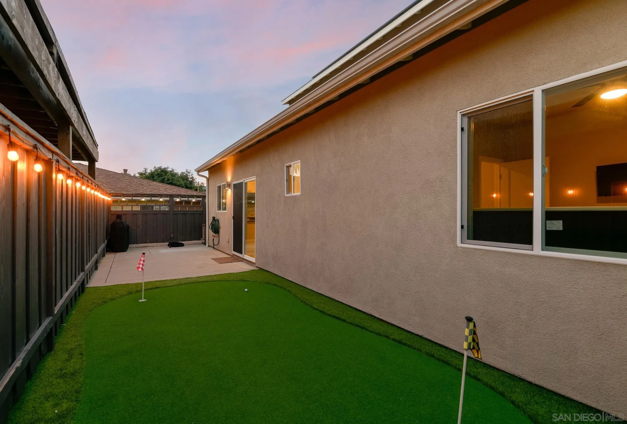 Backyard putting green with two golf flags beside the house at dusk.