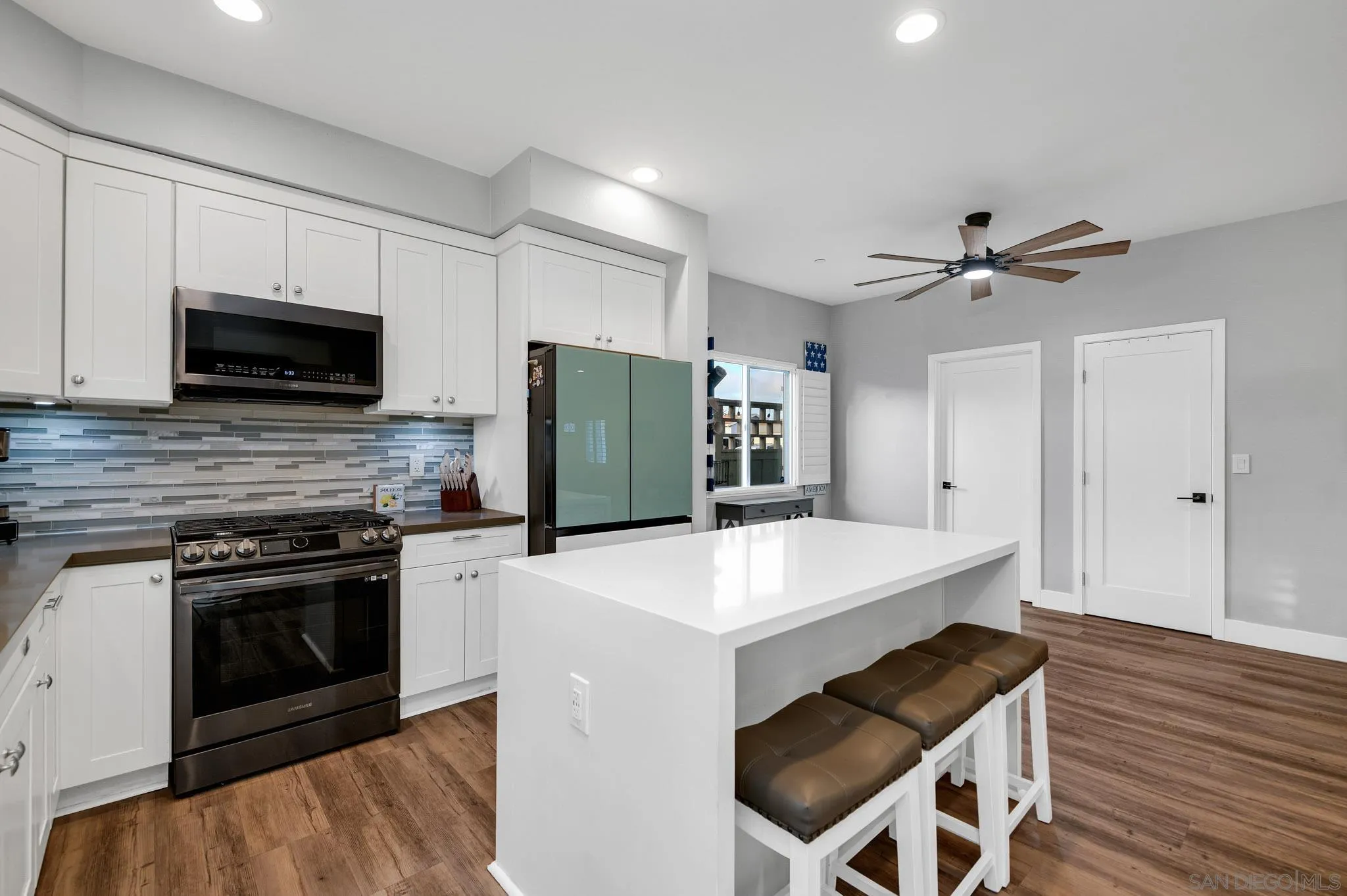 Kitchen with white cabinets, stainless steel range, green refrigerator, and a large island with cushioned stools.