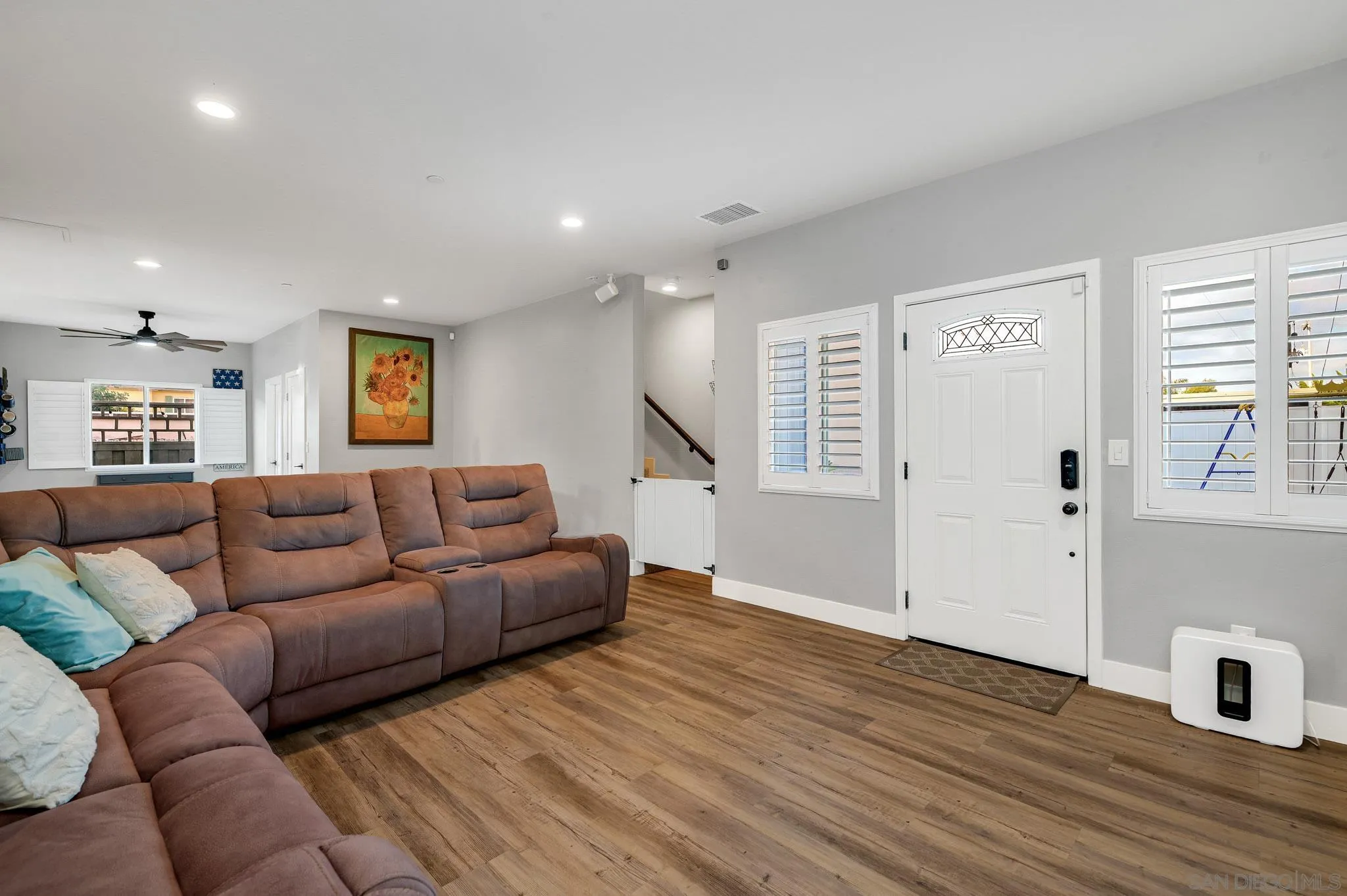 Living room with a brown sectional, wood-look floors, and a white front door with decorative glass.