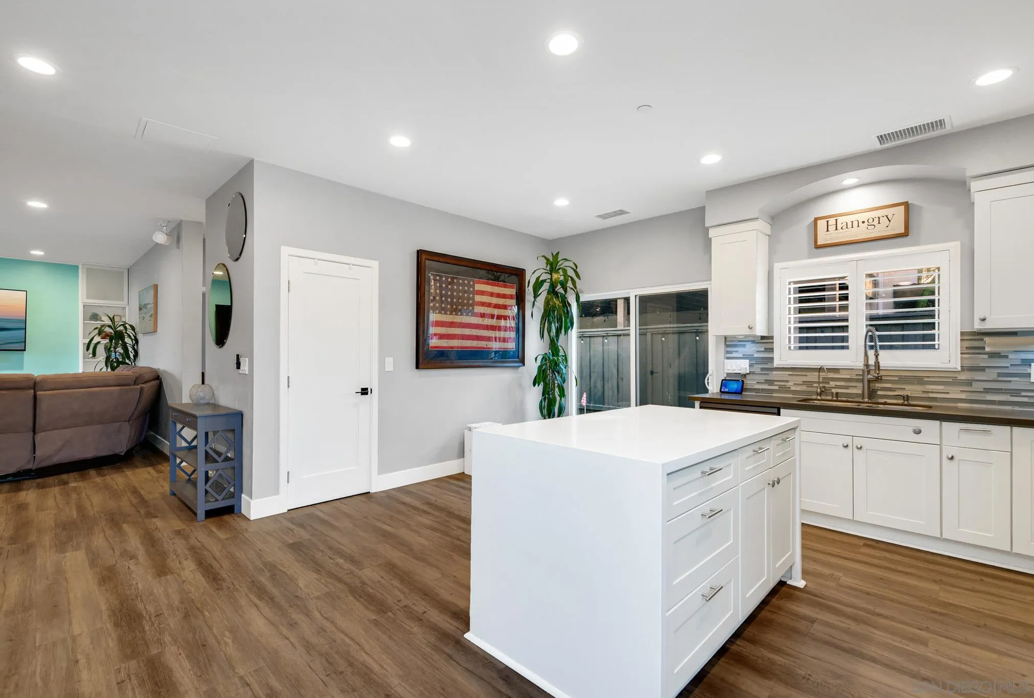 Open-plan kitchen with a large white island, white cabinetry, and wood-look flooring beside the living area.