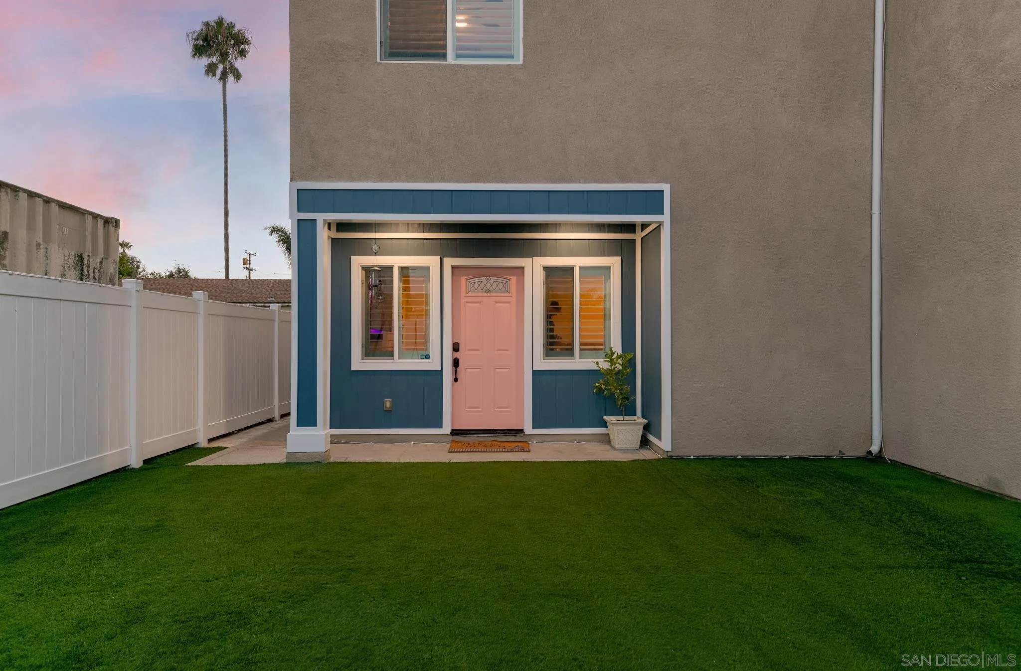 Home entrance with a pink front door, blue-and-white trim, green lawn, and white fence.