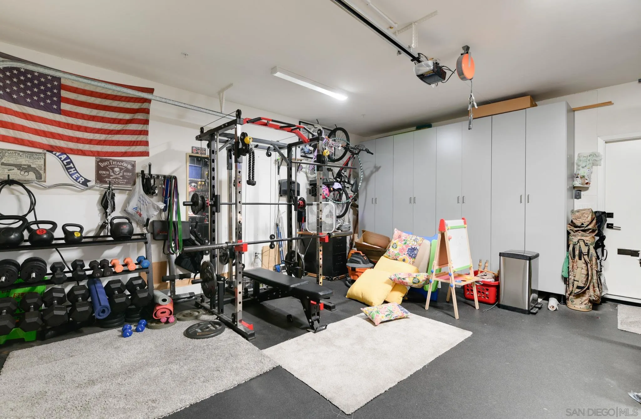 Garage gym with a power rack, weights, tall storage cabinets, and an American flag.