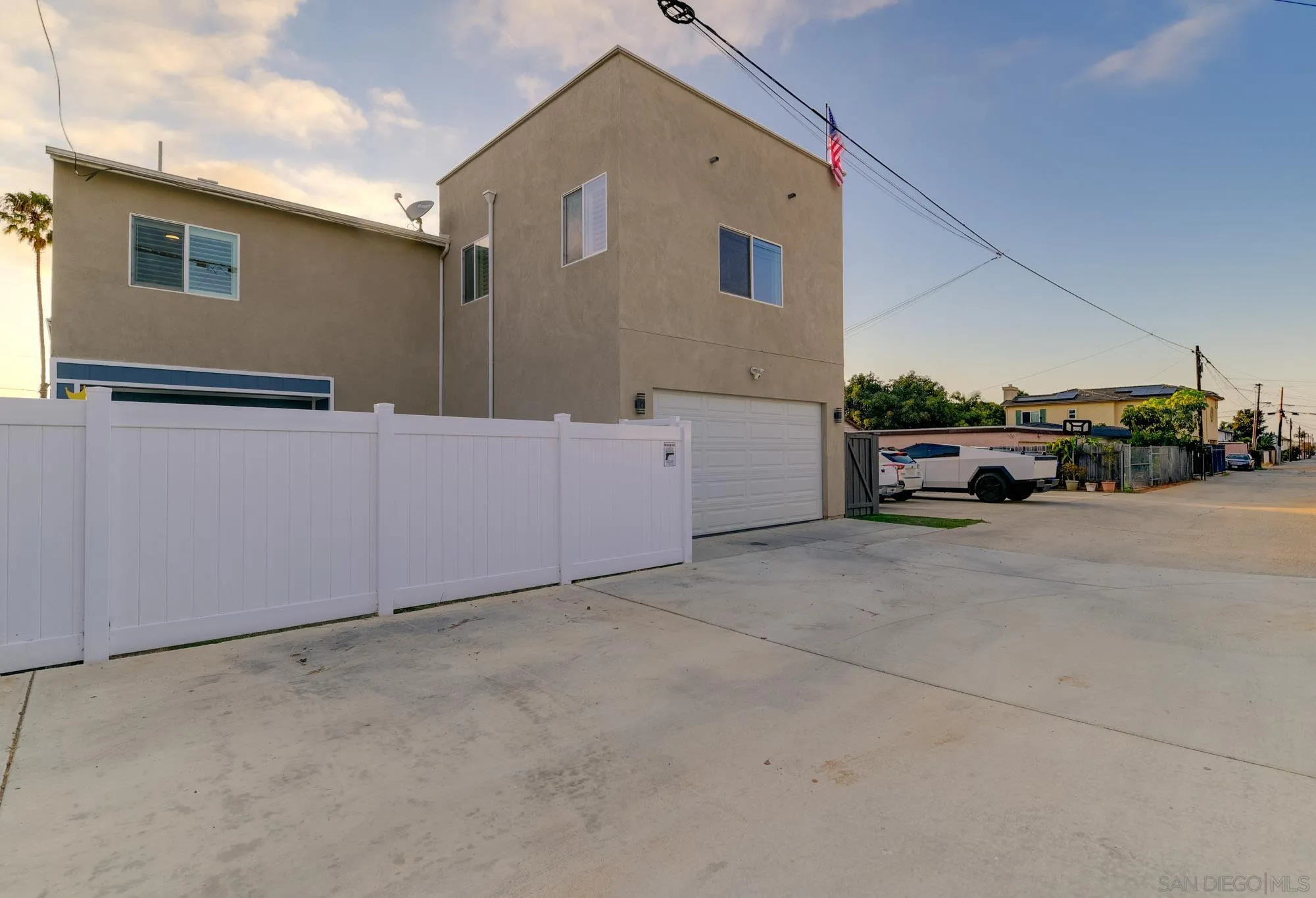 Two-story tan stucco house with a white privacy fence and wide driveway.