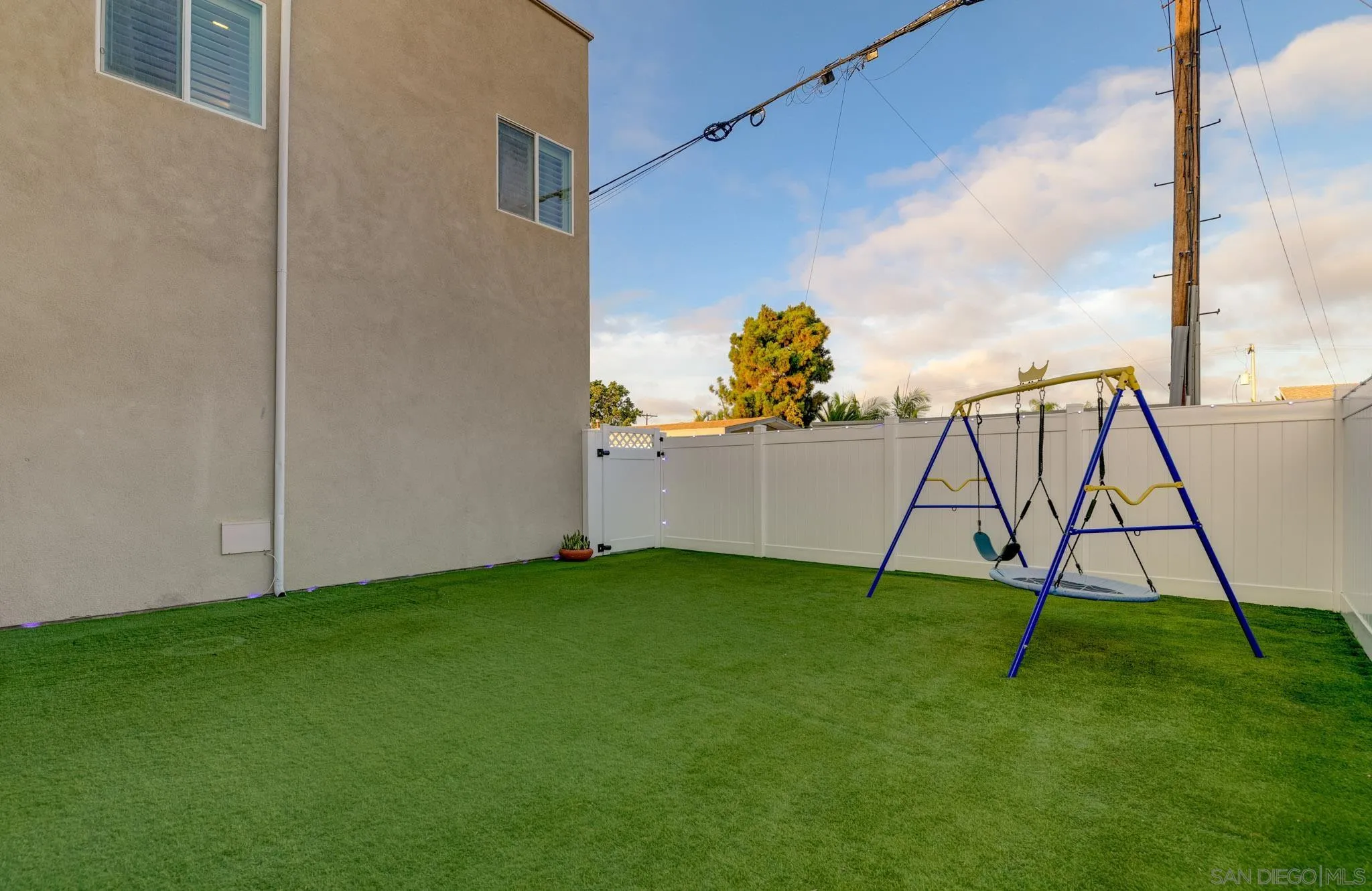 Fenced backyard with artificial turf and a blue-and-yellow swing set.