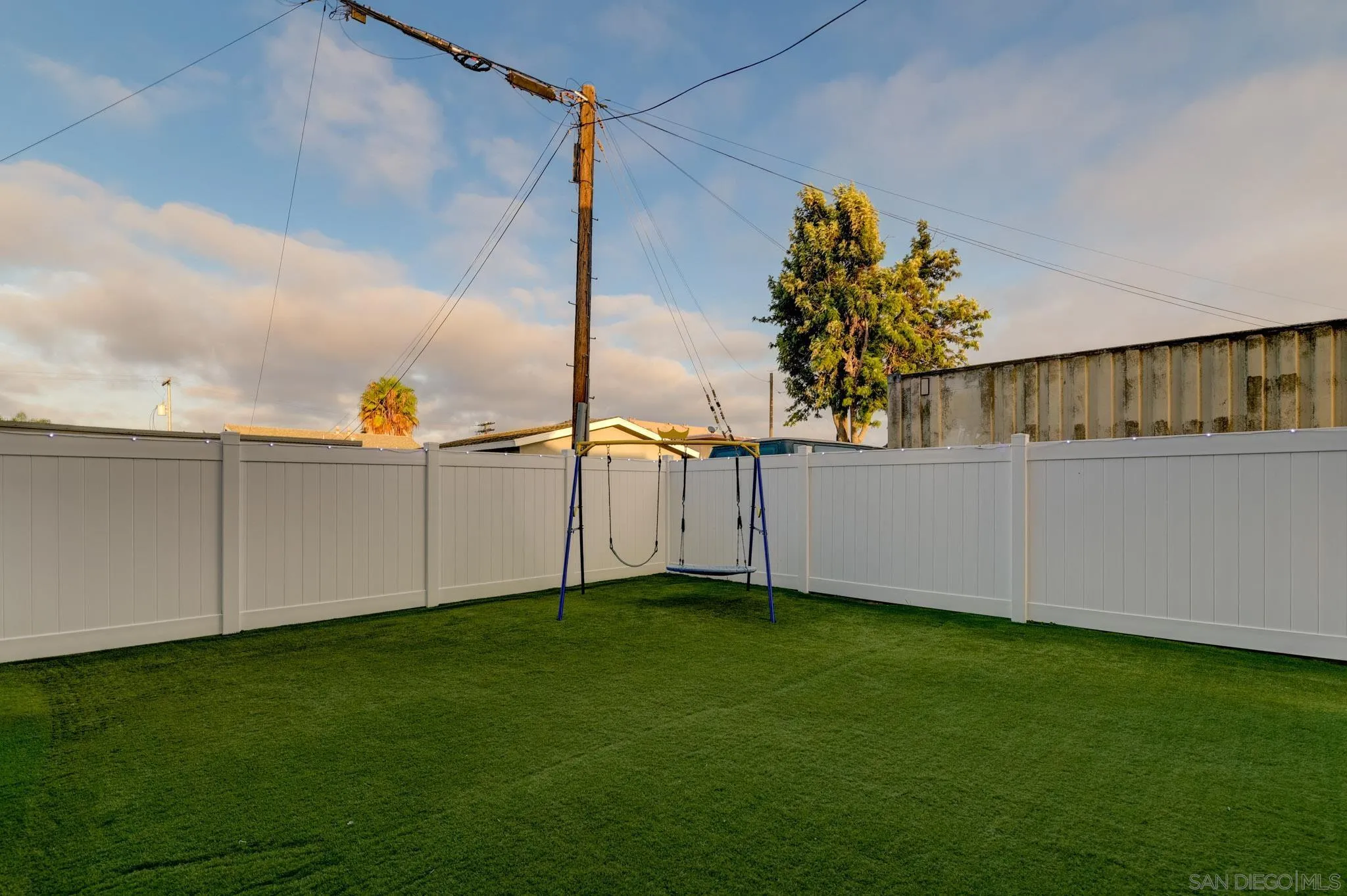 Fenced backyard with green artificial turf and a blue swing set.