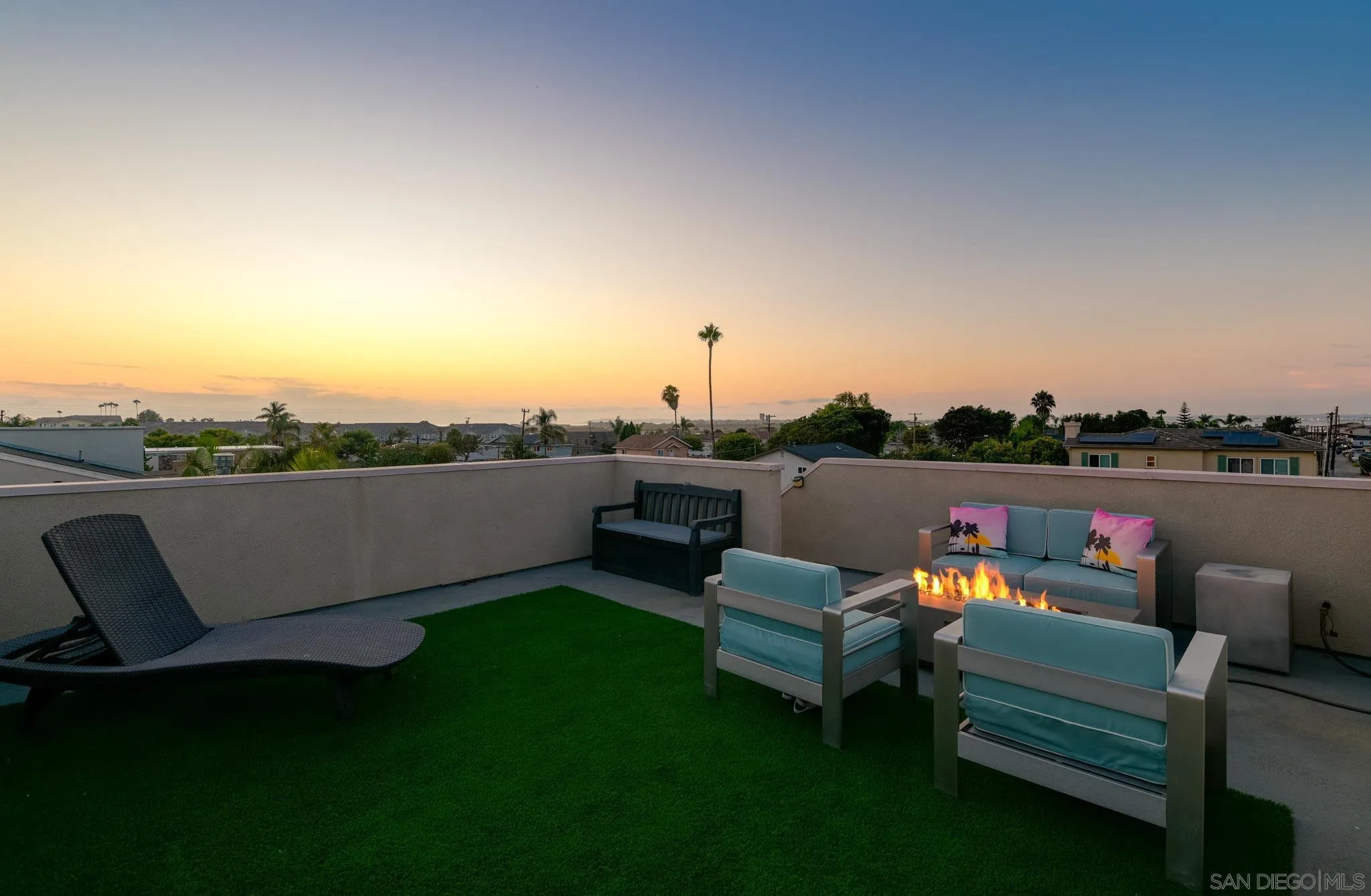 Rooftop terrace with lounge seating and a lit fire feature at sunset.