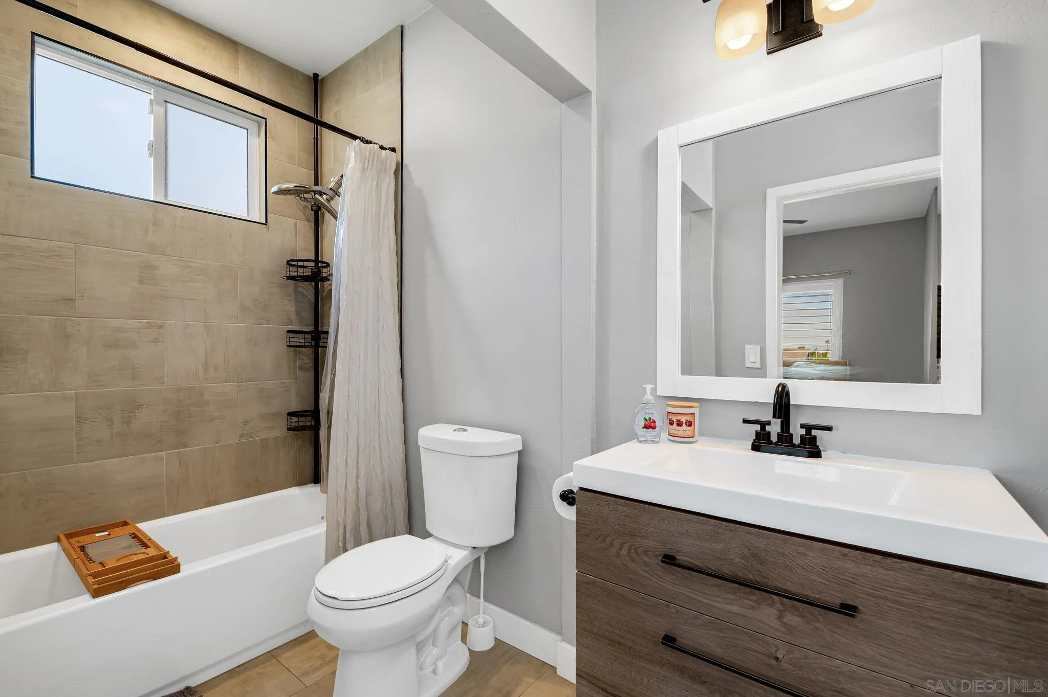 Bathroom with beige tiled tub surround, high window, and dark wood vanity with black fixtures.
