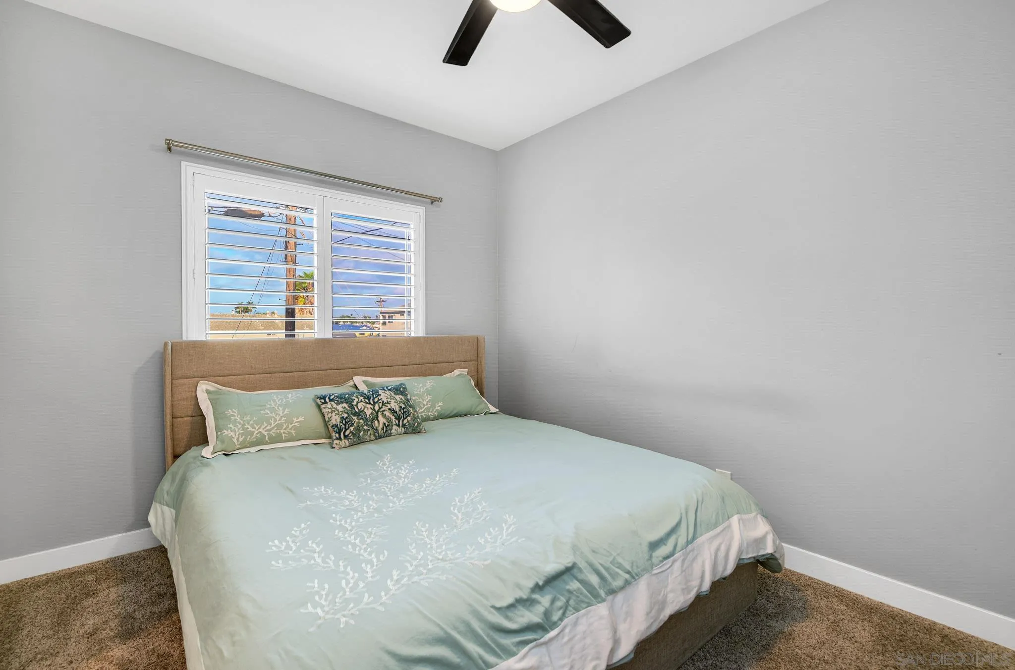 Bedroom with pale aqua patterned bedding and white plantation shutters overlooking blue sky.