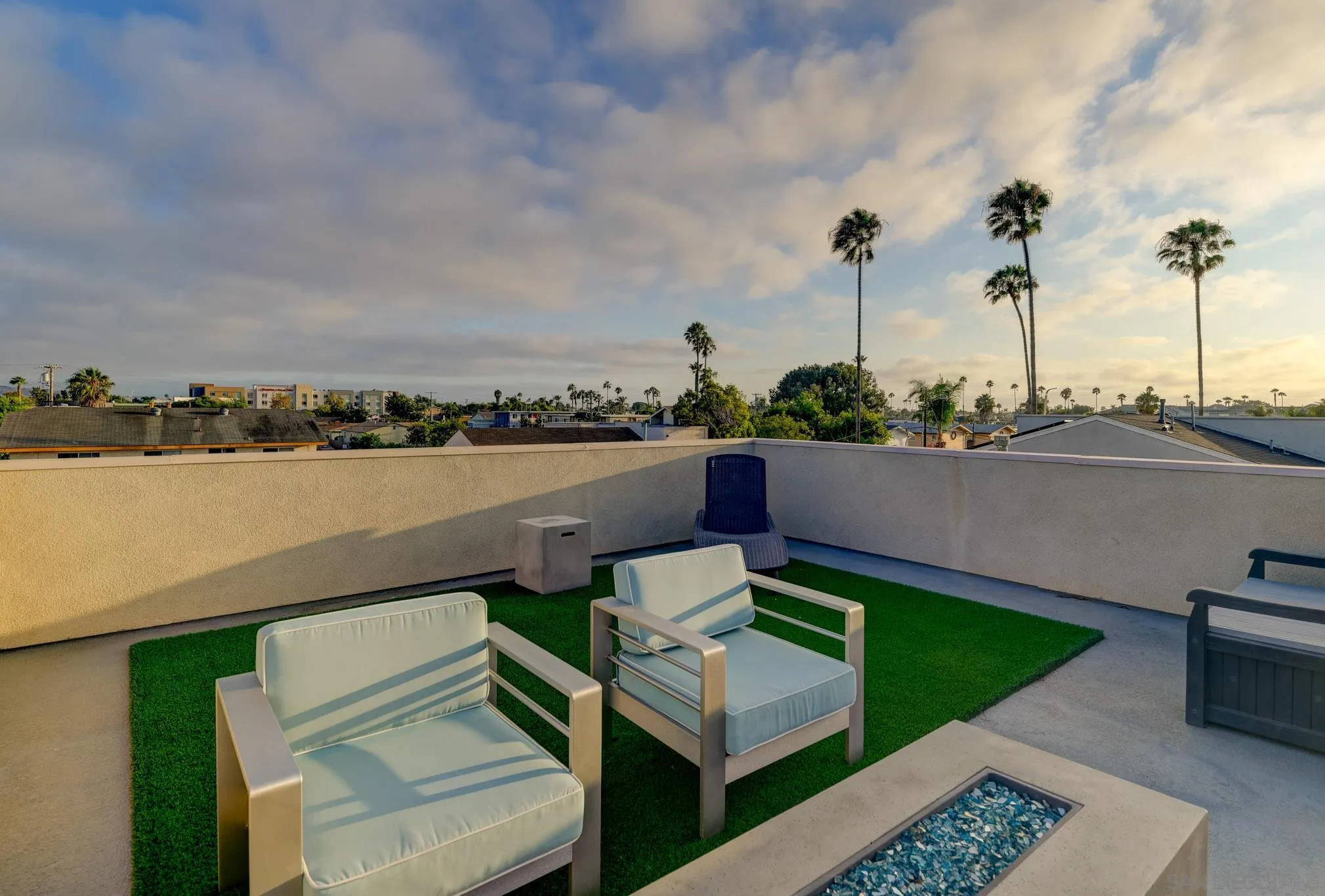 Rooftop patio with lounge chairs, artificial turf, a fire feature, and palm-lined neighborhood views.