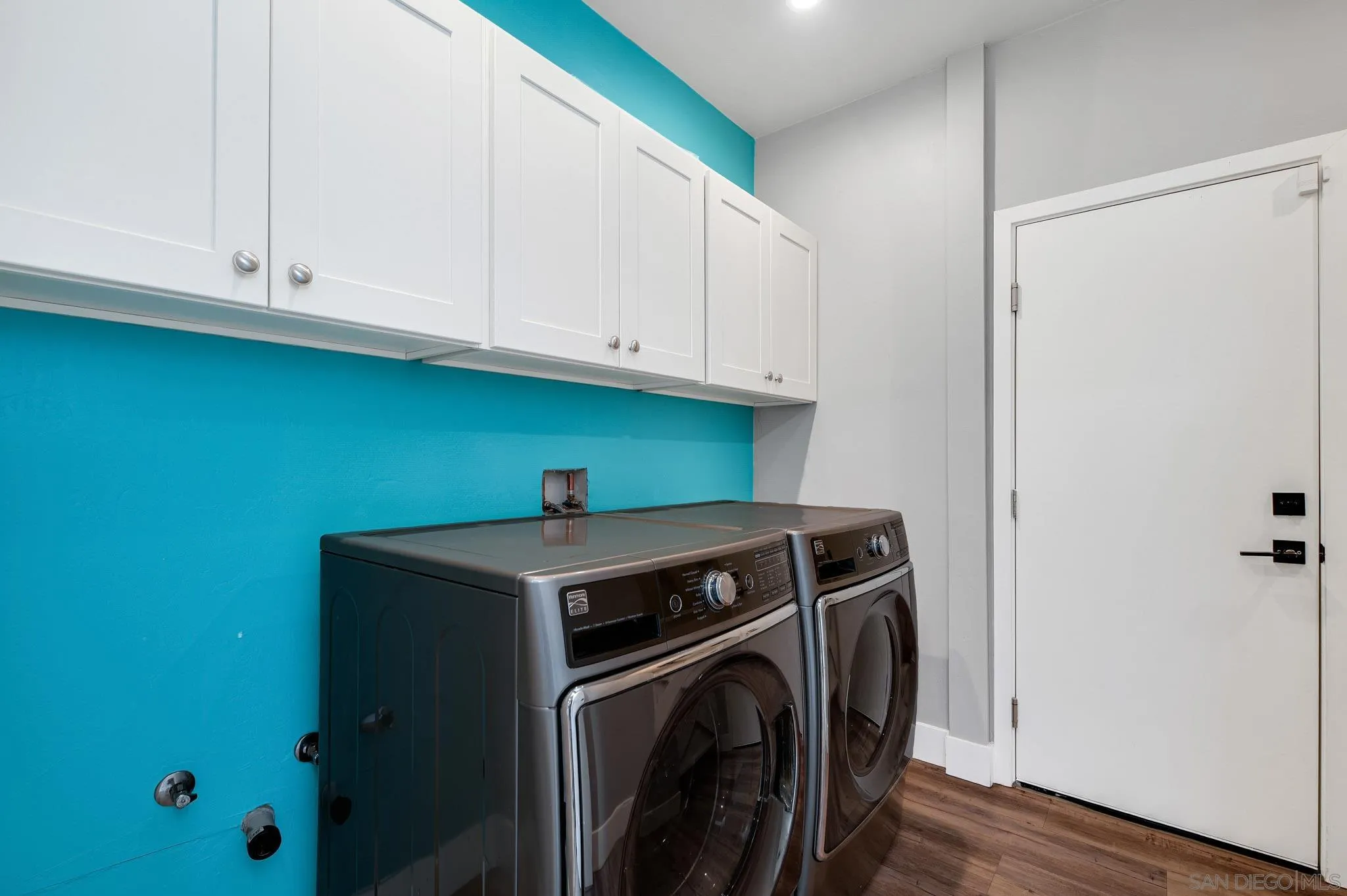 Laundry room with front-loading washer and dryer, white cabinets, and a turquoise accent wall.