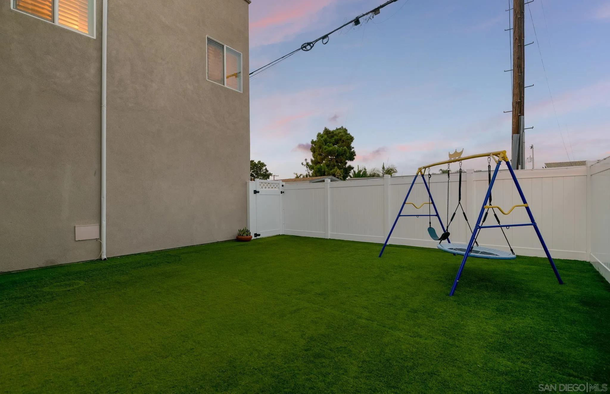 Fenced backyard with artificial turf and a blue-and-yellow swing set.