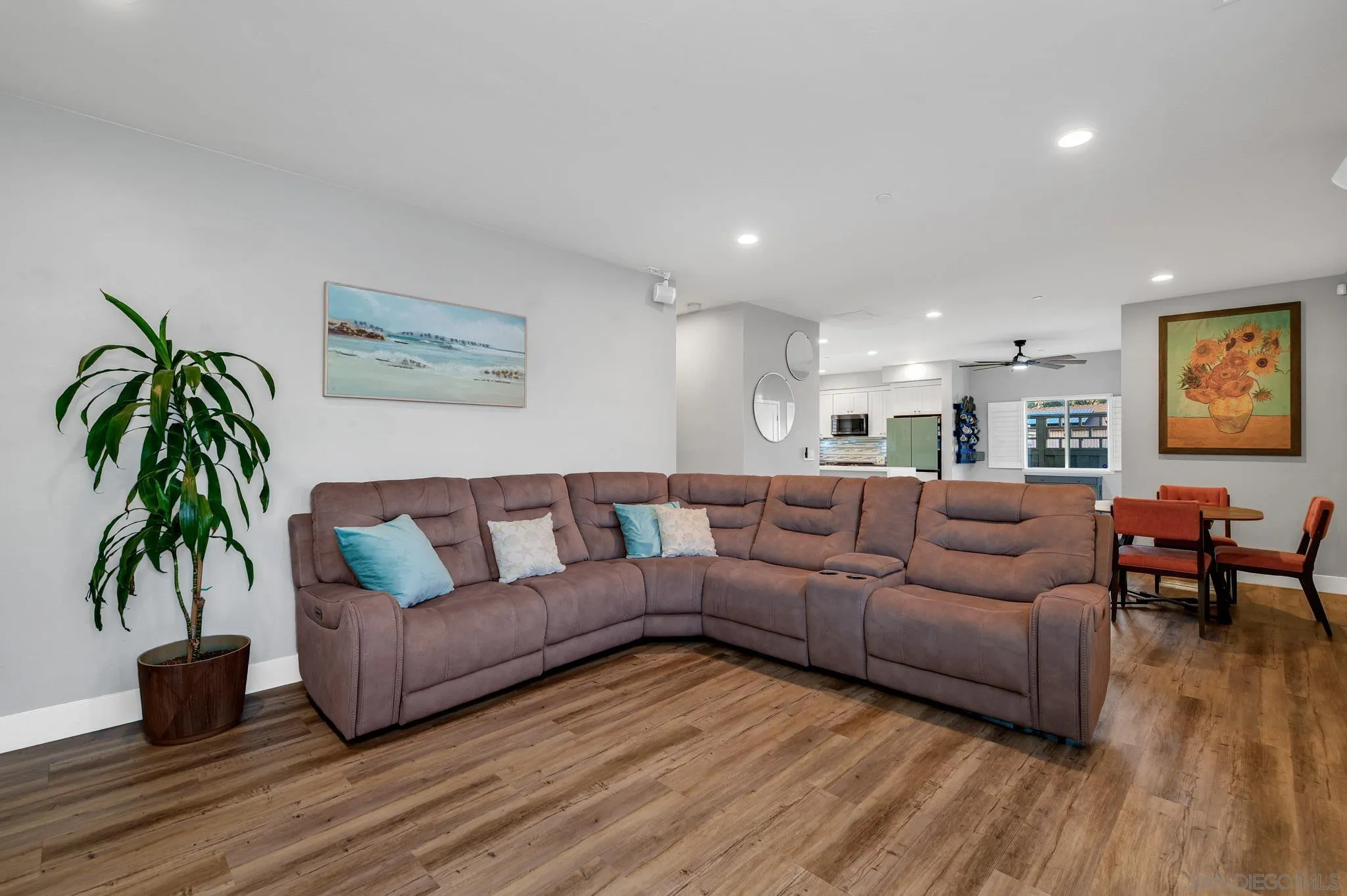 Living room with a large mauve sectional sofa, wood-look floors, and an open kitchen and dining area.