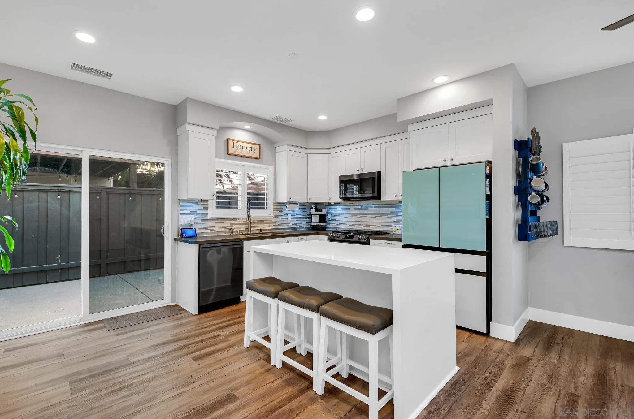 Kitchen with white cabinetry, a large island with three stools, and a turquoise refrigerator.