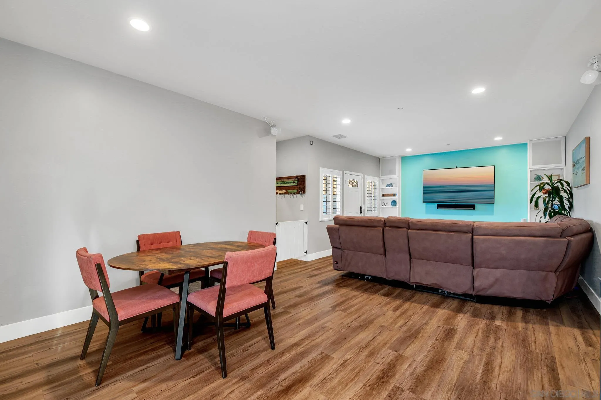 Open-plan living and dining room with a brown sectional, turquoise TV wall, and round table with coral chairs.