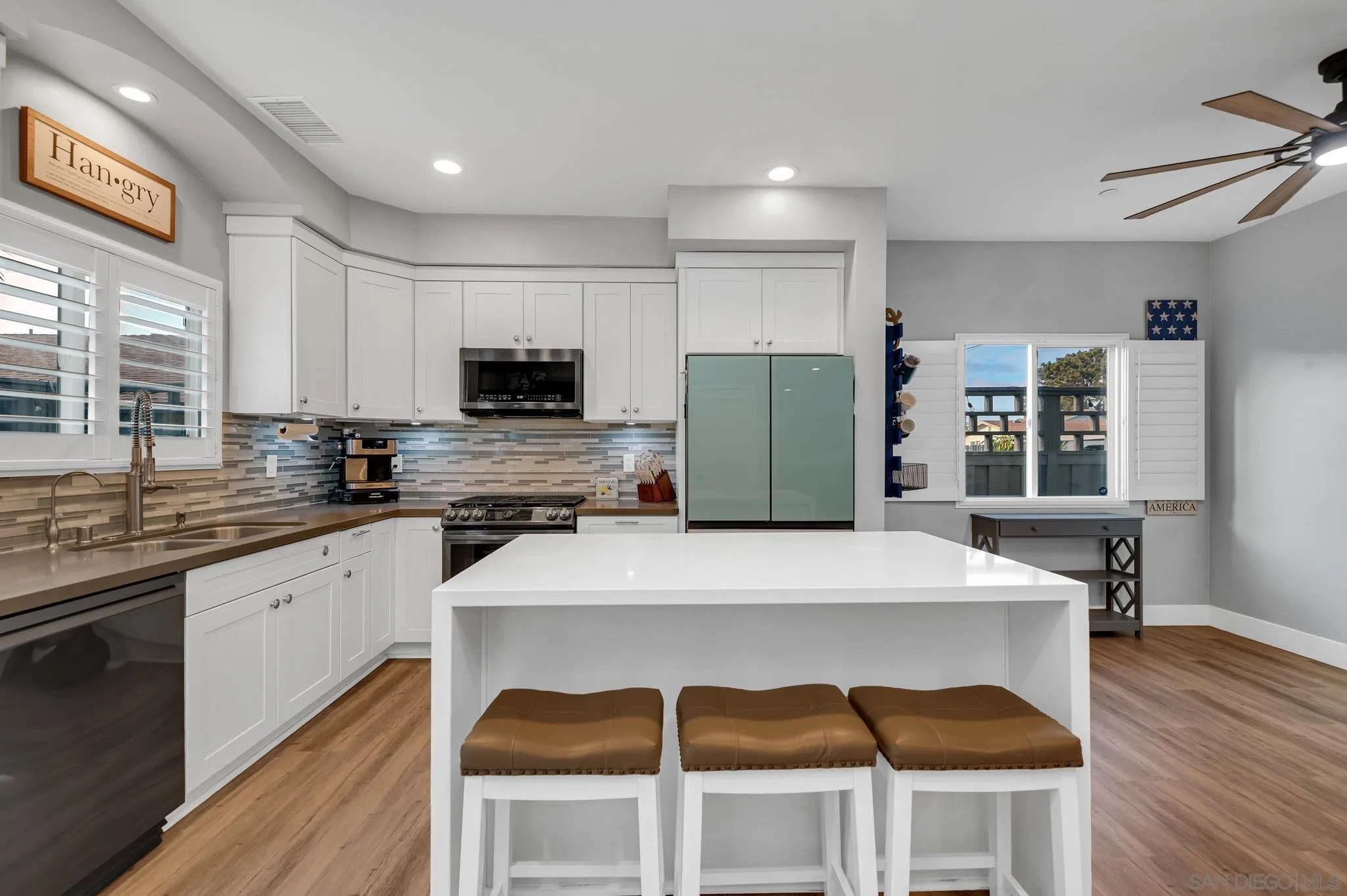 Kitchen with a large white island, three stools, white cabinetry, and shuttered windows.