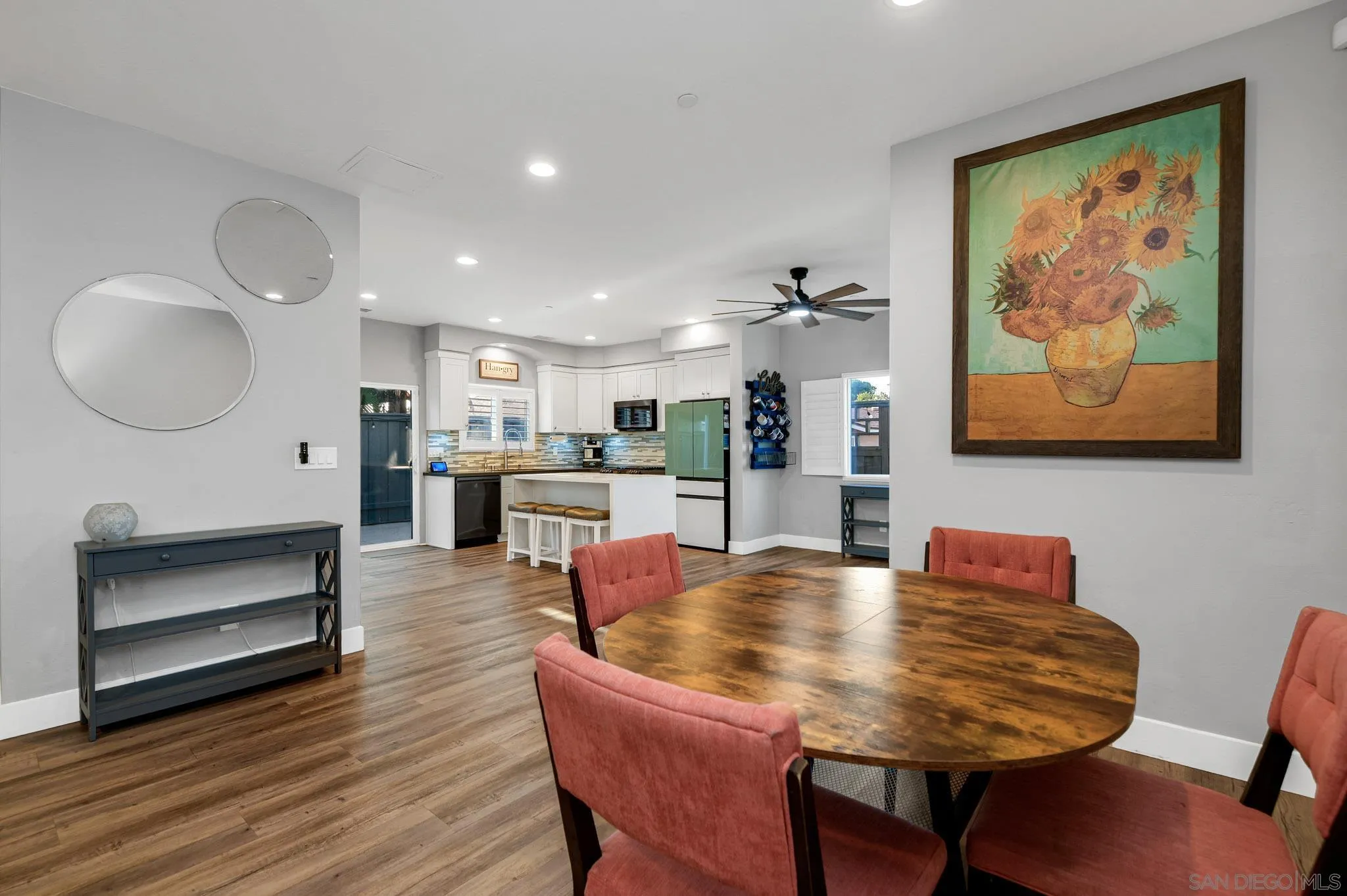 Dining area with a round wood table and coral chairs beside an open white kitchen.