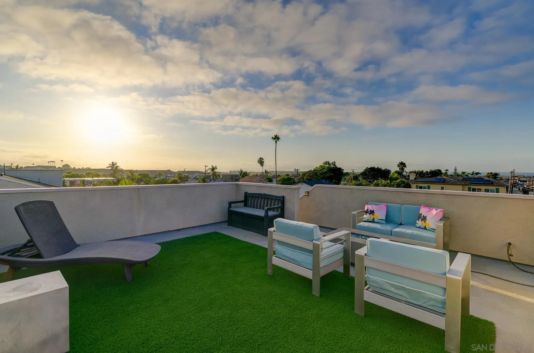 Rooftop deck with artificial grass, outdoor seating, and sunset views over the neighborhood.