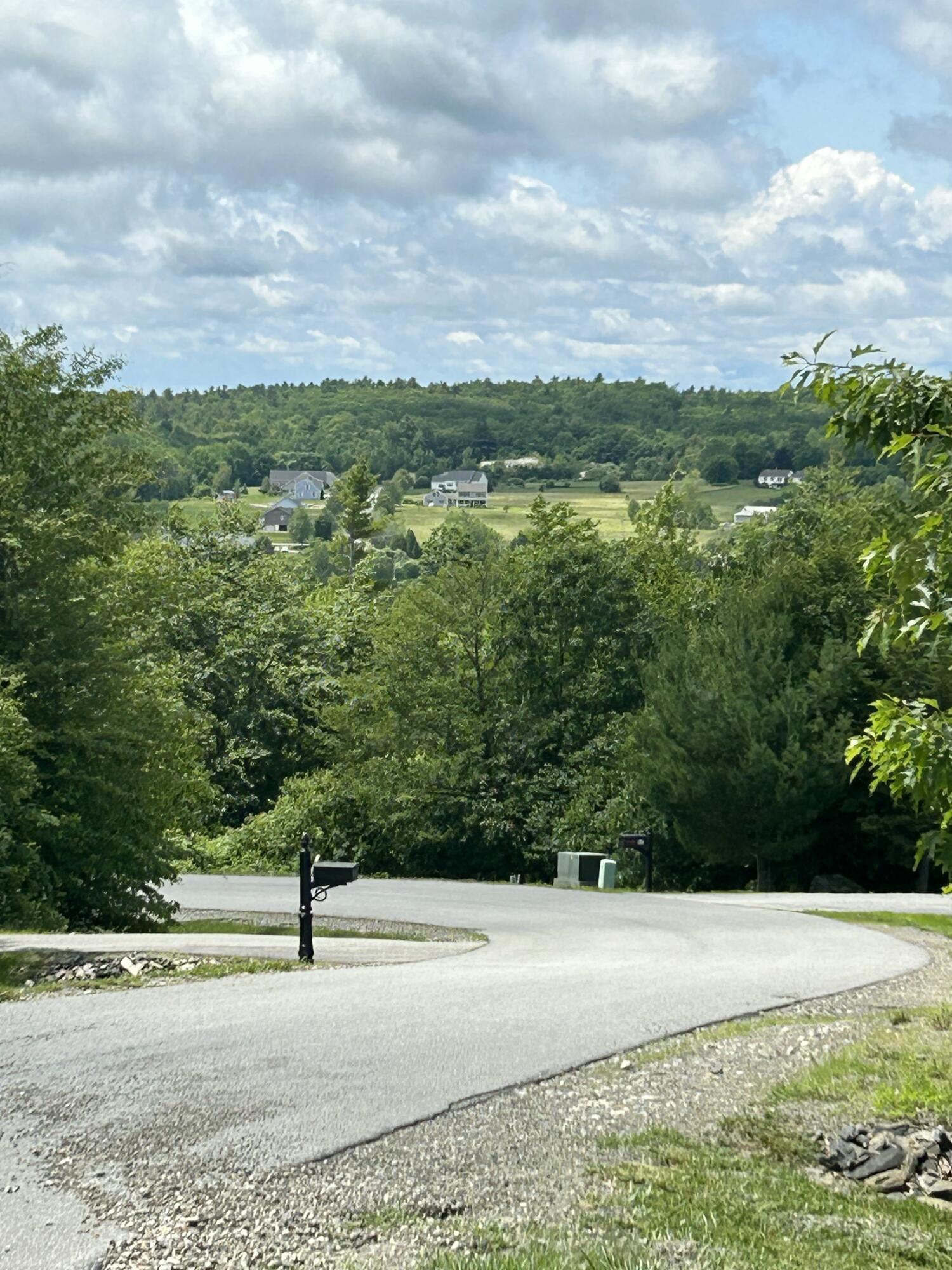A curving road and mailbox overlook wooded hills, open fields, and scattered homes.