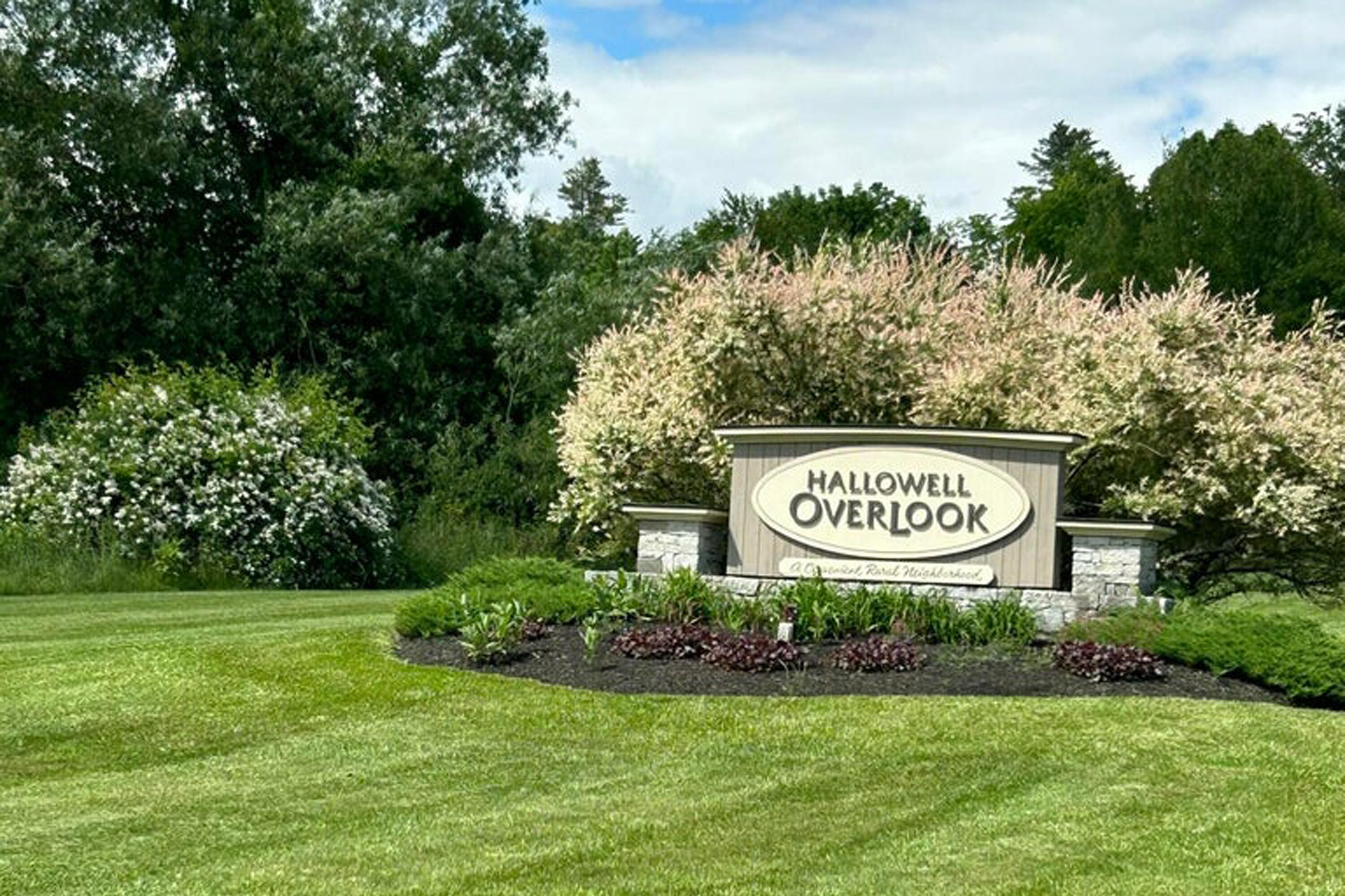Hallowell Overlook entrance sign surrounded by flowering shrubs and a manicured lawn.
