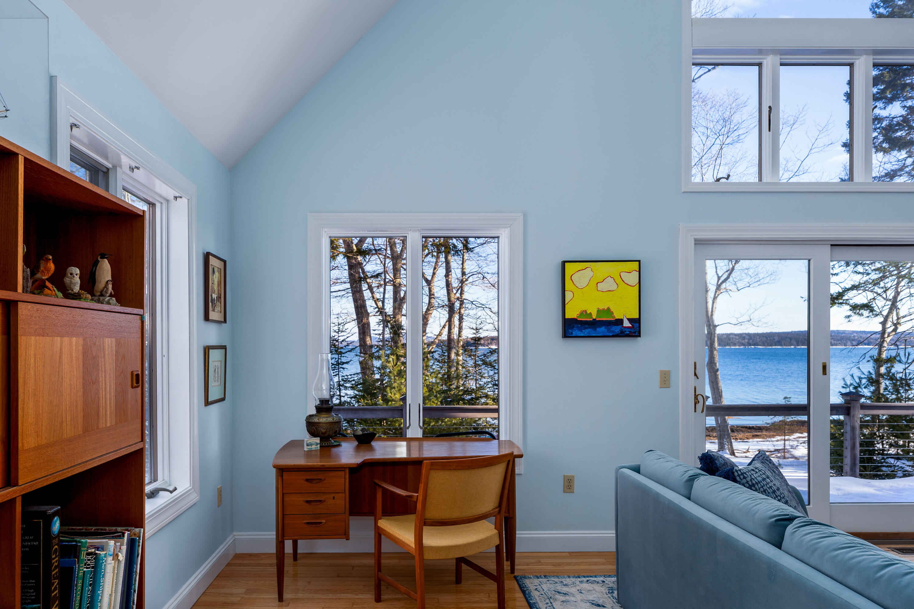 Living room with a wooden desk and sofa overlooking a snowy waterfront.
