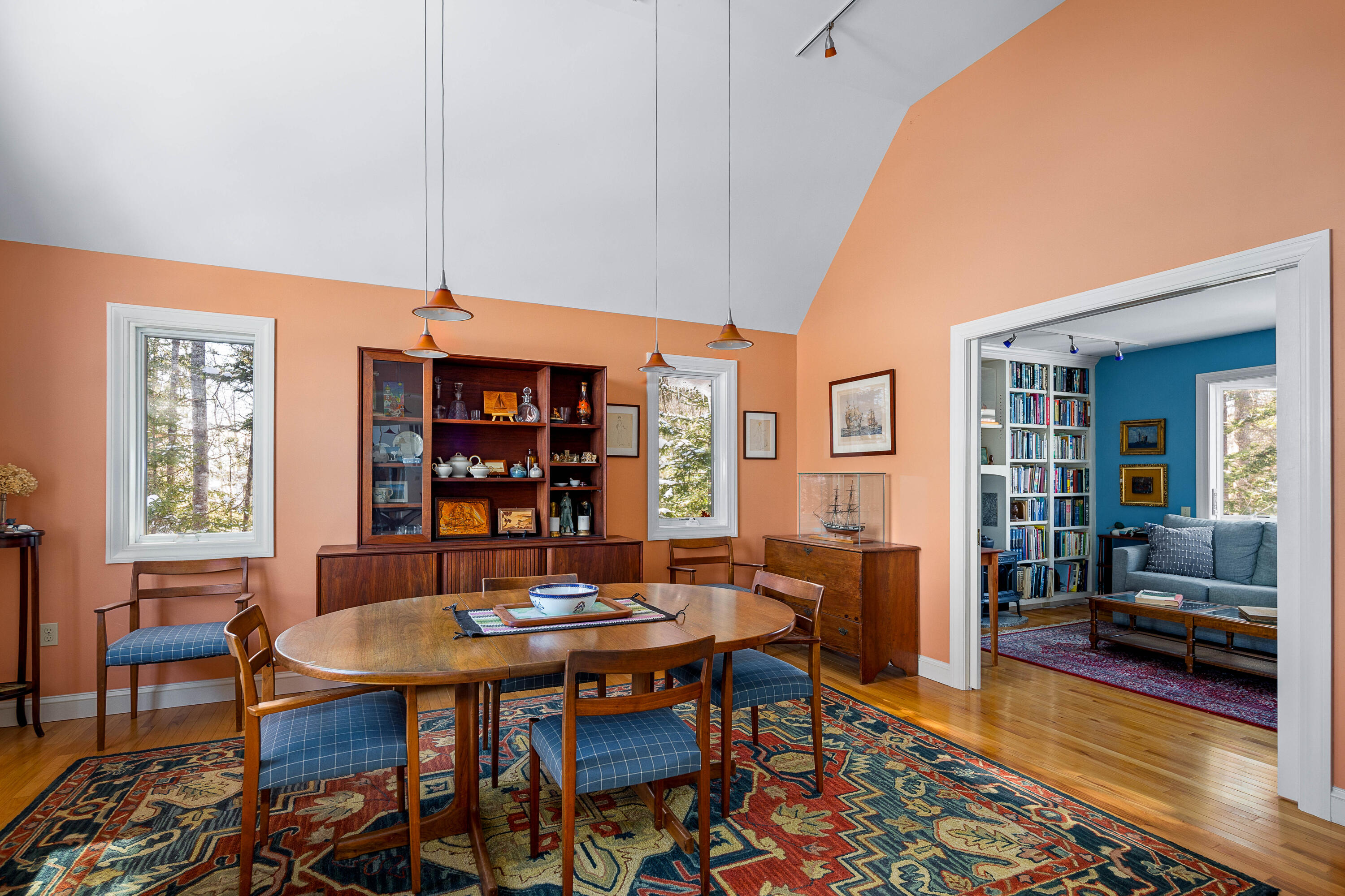 Dining room with peach walls, a wooden table, patterned rug, and doorway to a blue-walled sitting room.