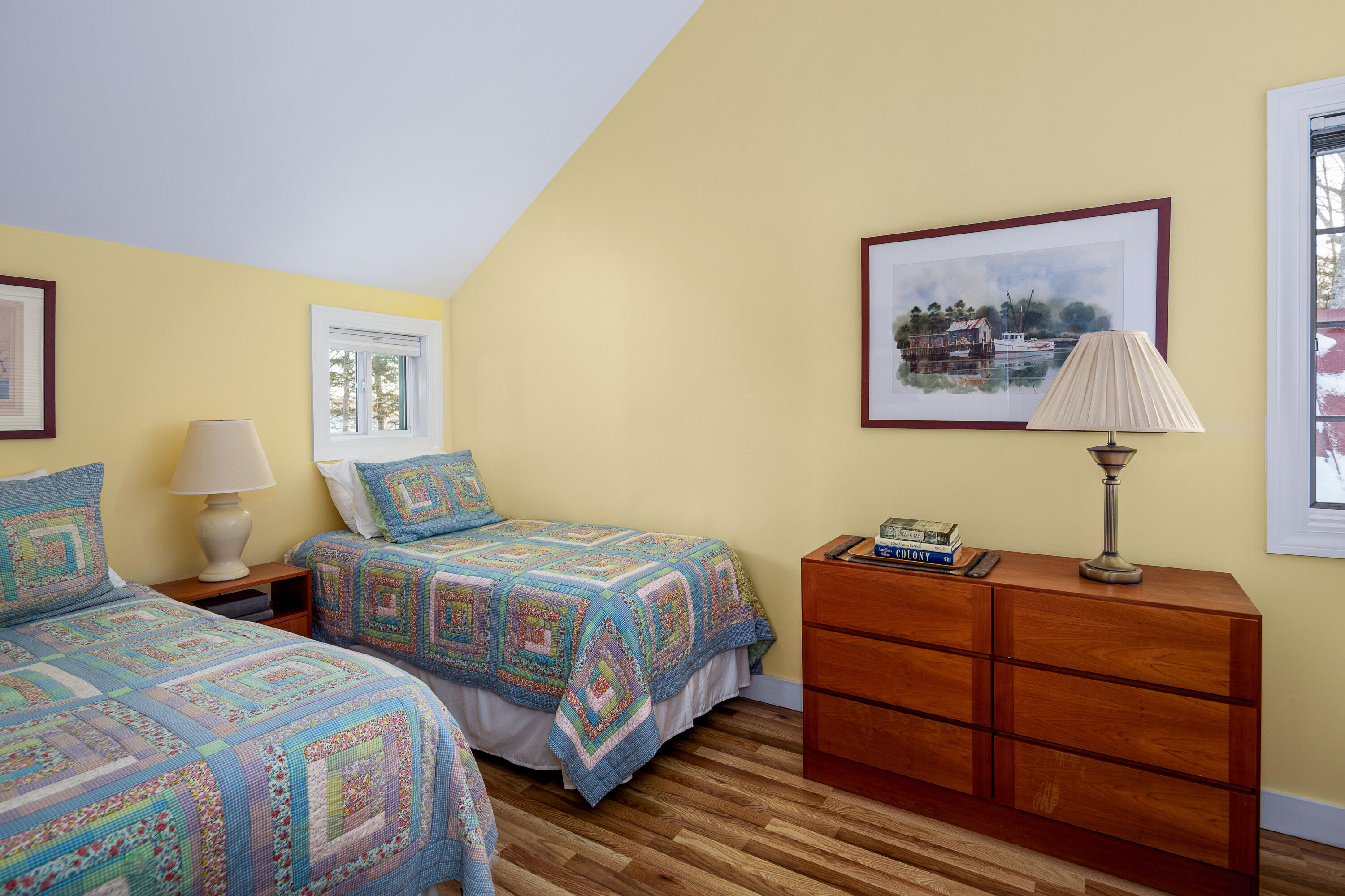 Bedroom with two twin beds in colorful patchwork quilts and a wooden dresser.