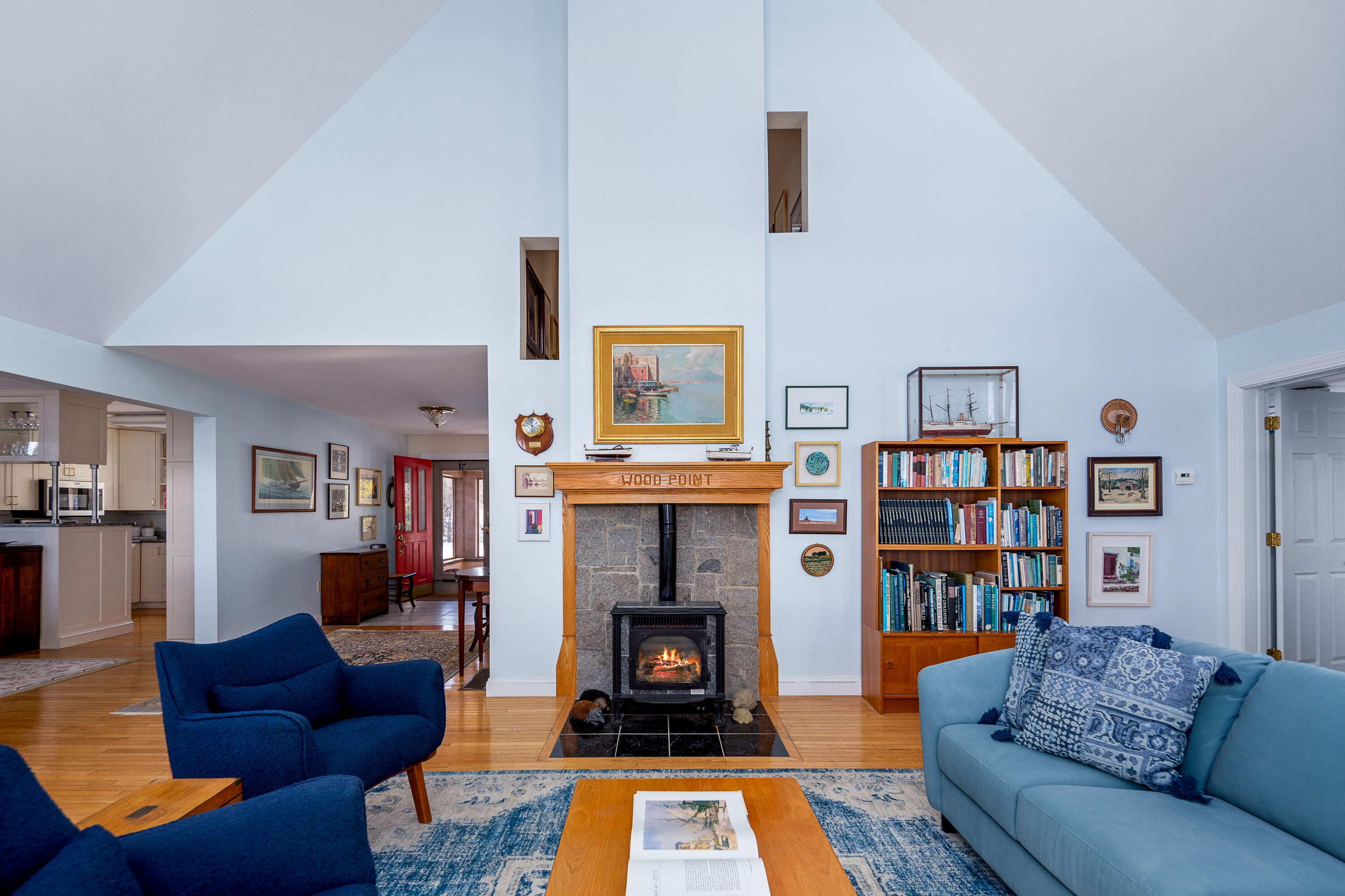 Living room with vaulted ceilings, blue seating, and a stone fireplace with a burning wood stove.