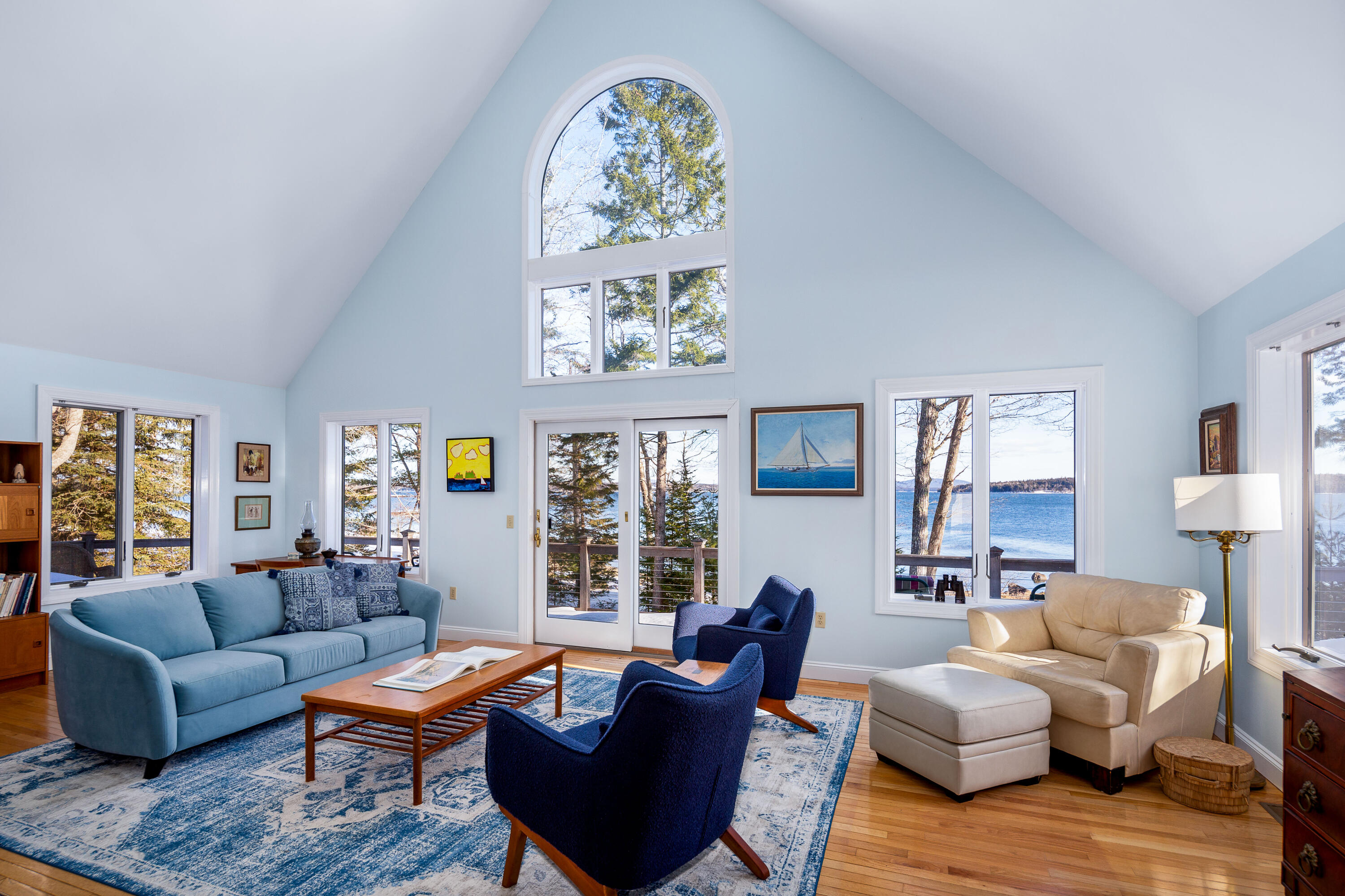 Living room with a vaulted ceiling, large water-view windows, and blue and cream seating.