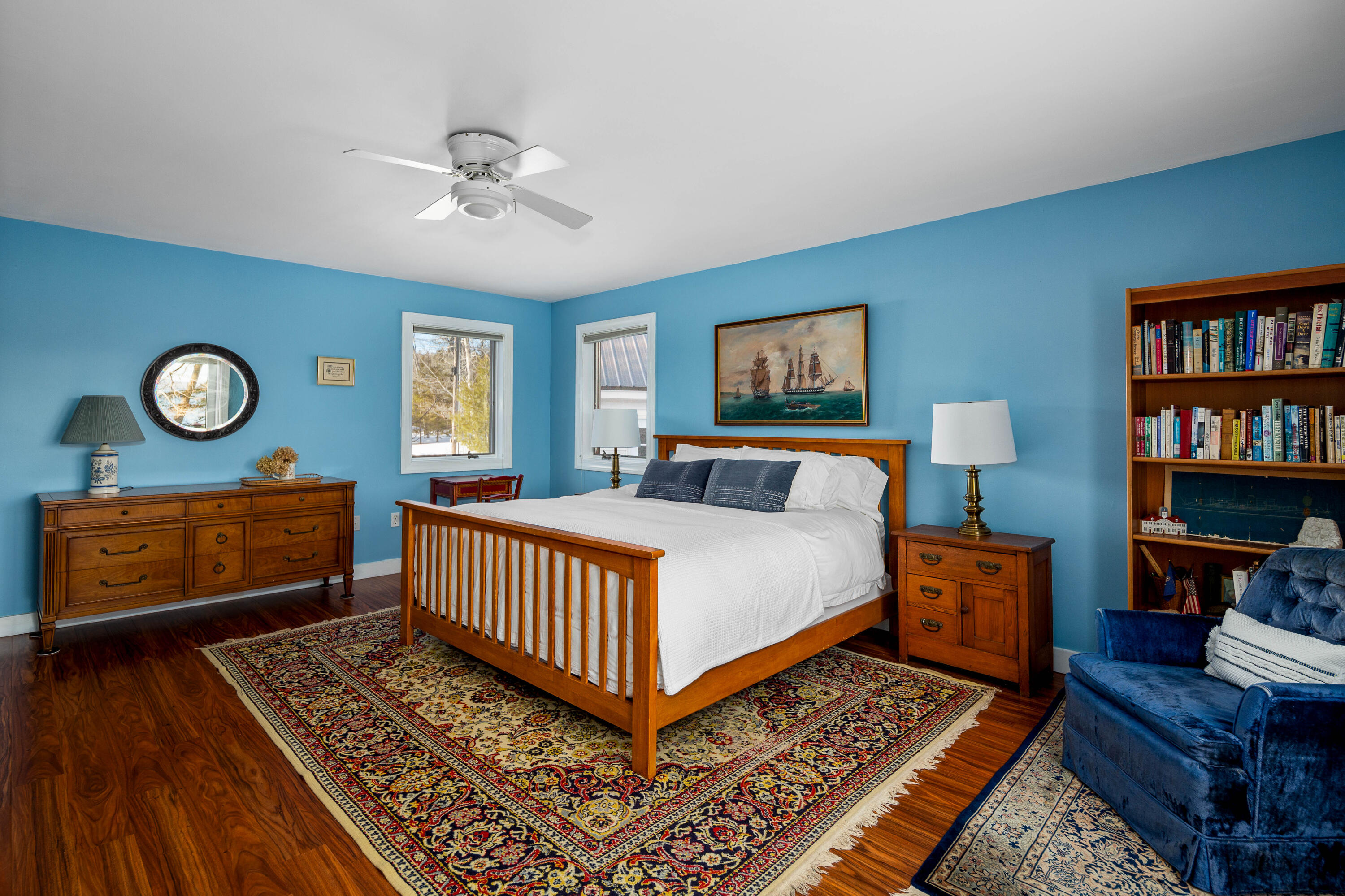Blue bedroom with a wooden bed, patterned rugs, and a tall bookcase.